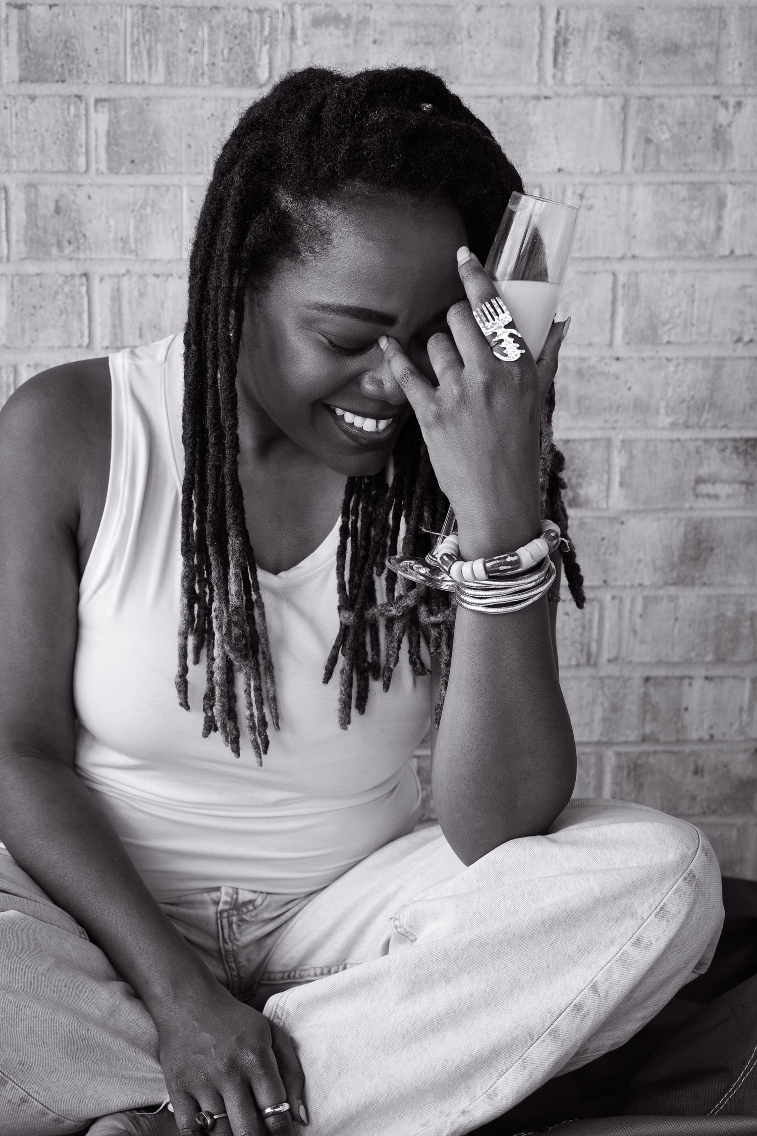Black-and-white photo of a woman with dreadlocks chuckling as she holds a glass of champagne.