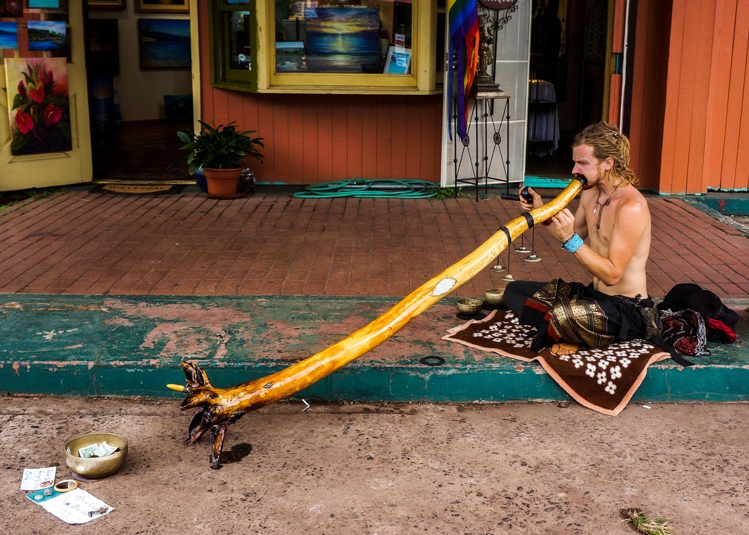 A musician on a street corner blows hard into a wooden horn.