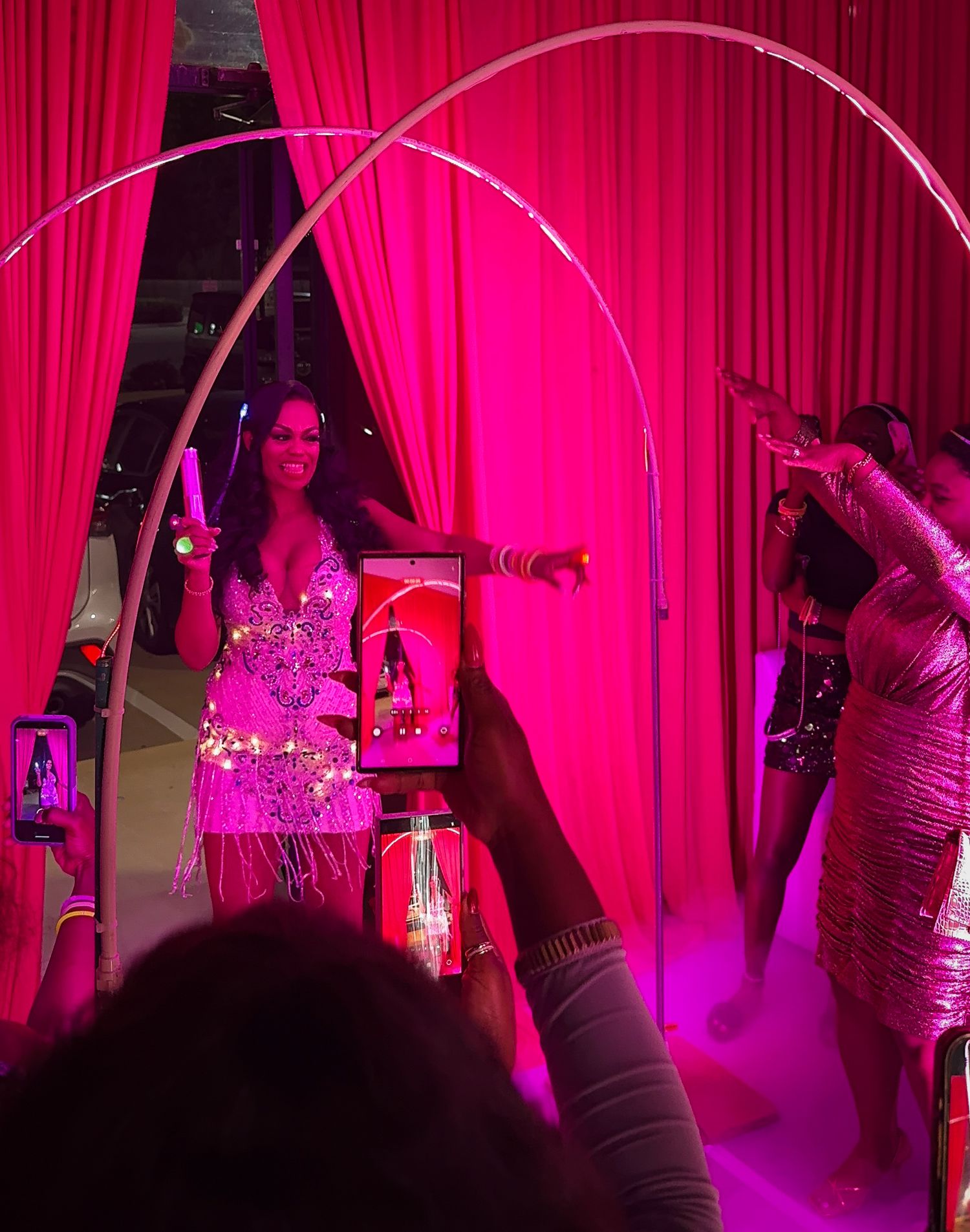 An excited woman dances into a party, bathed in pink light.