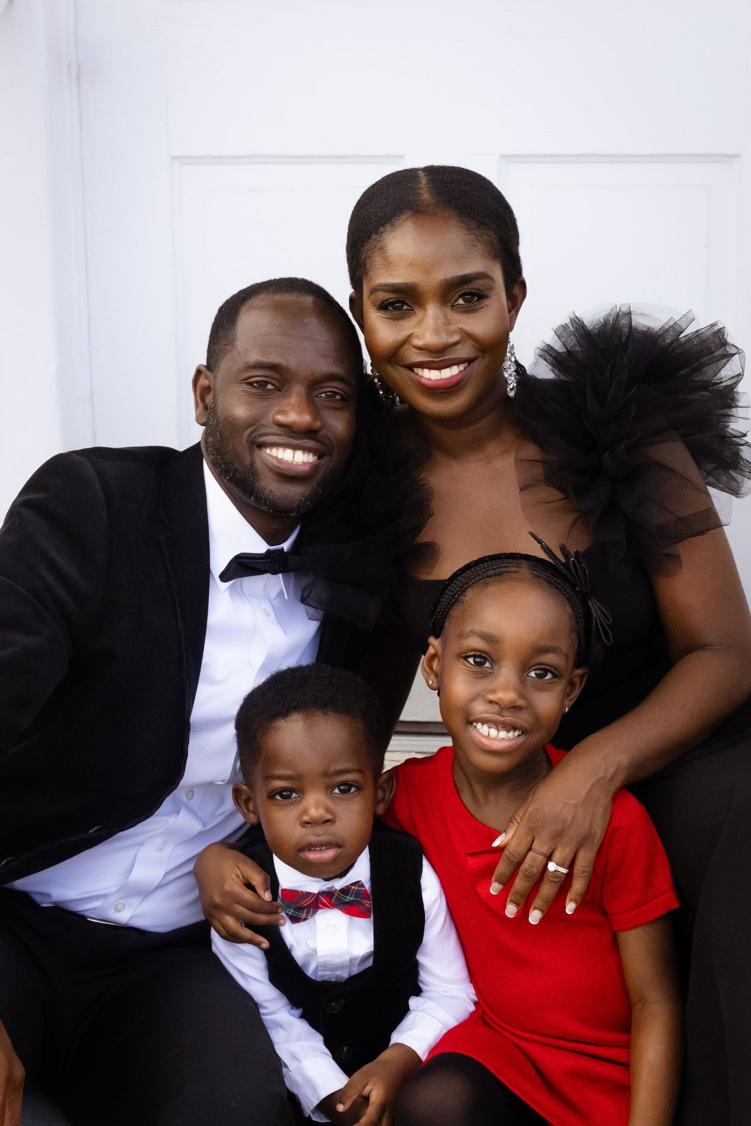 An elegantly dressed family of four huddles together and smiles for the camera.