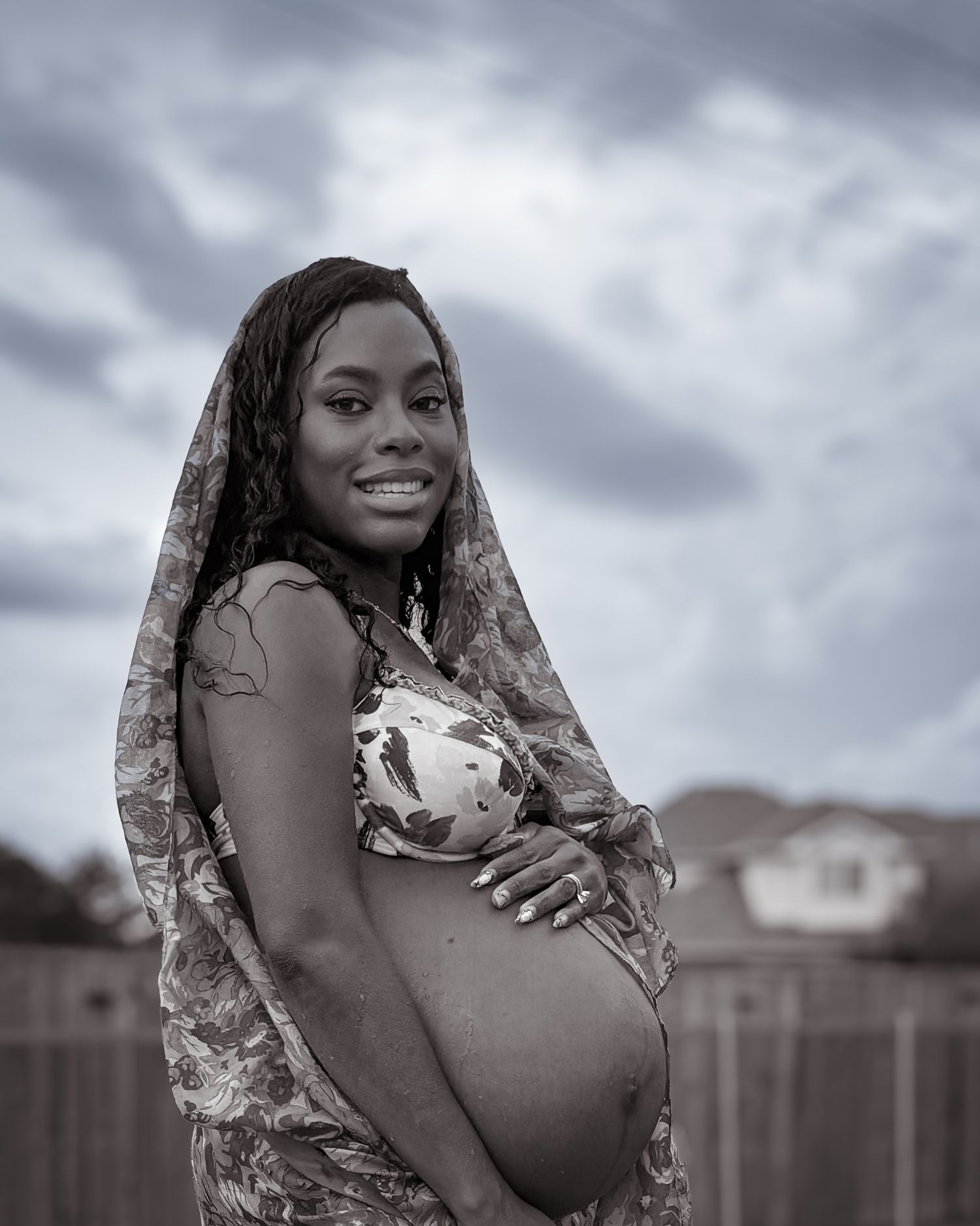 A pregnant woman with wet hair under a scarf caresses her belly and smiles at the camera.