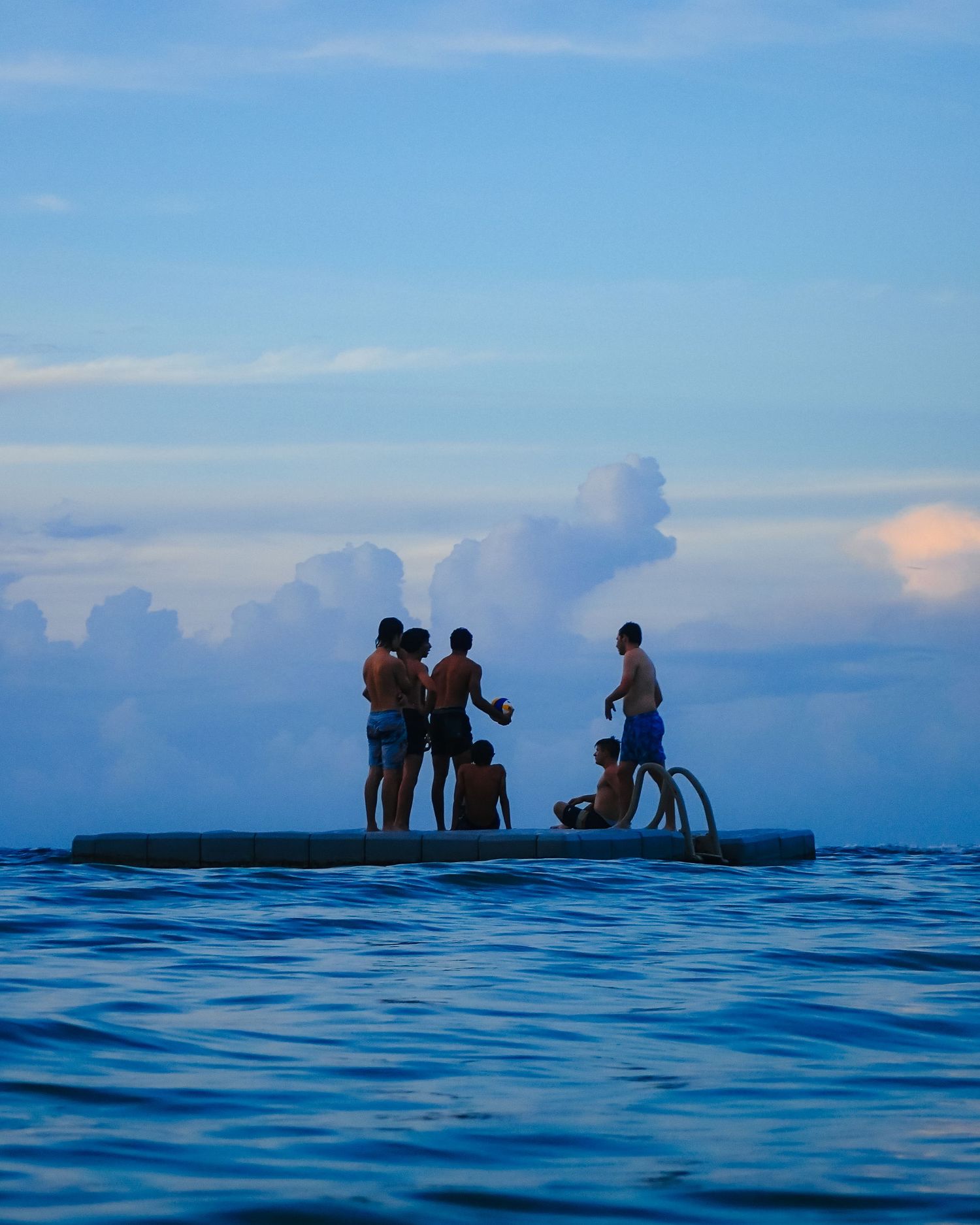 Teenage boys gather on a floating platform out at sea.