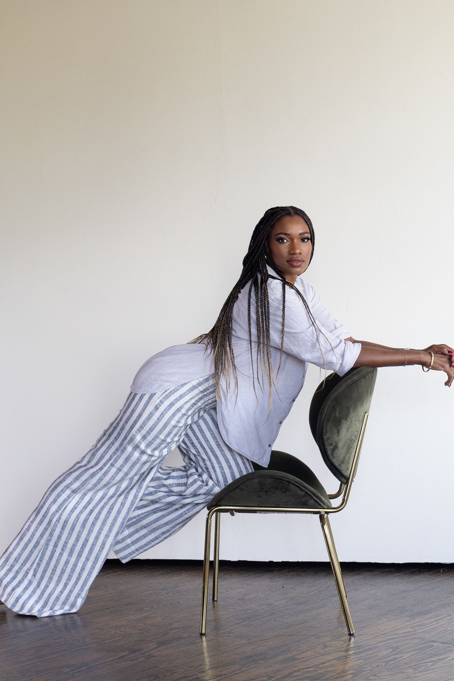 A woman in bright white clothes leans on a green velvet chair