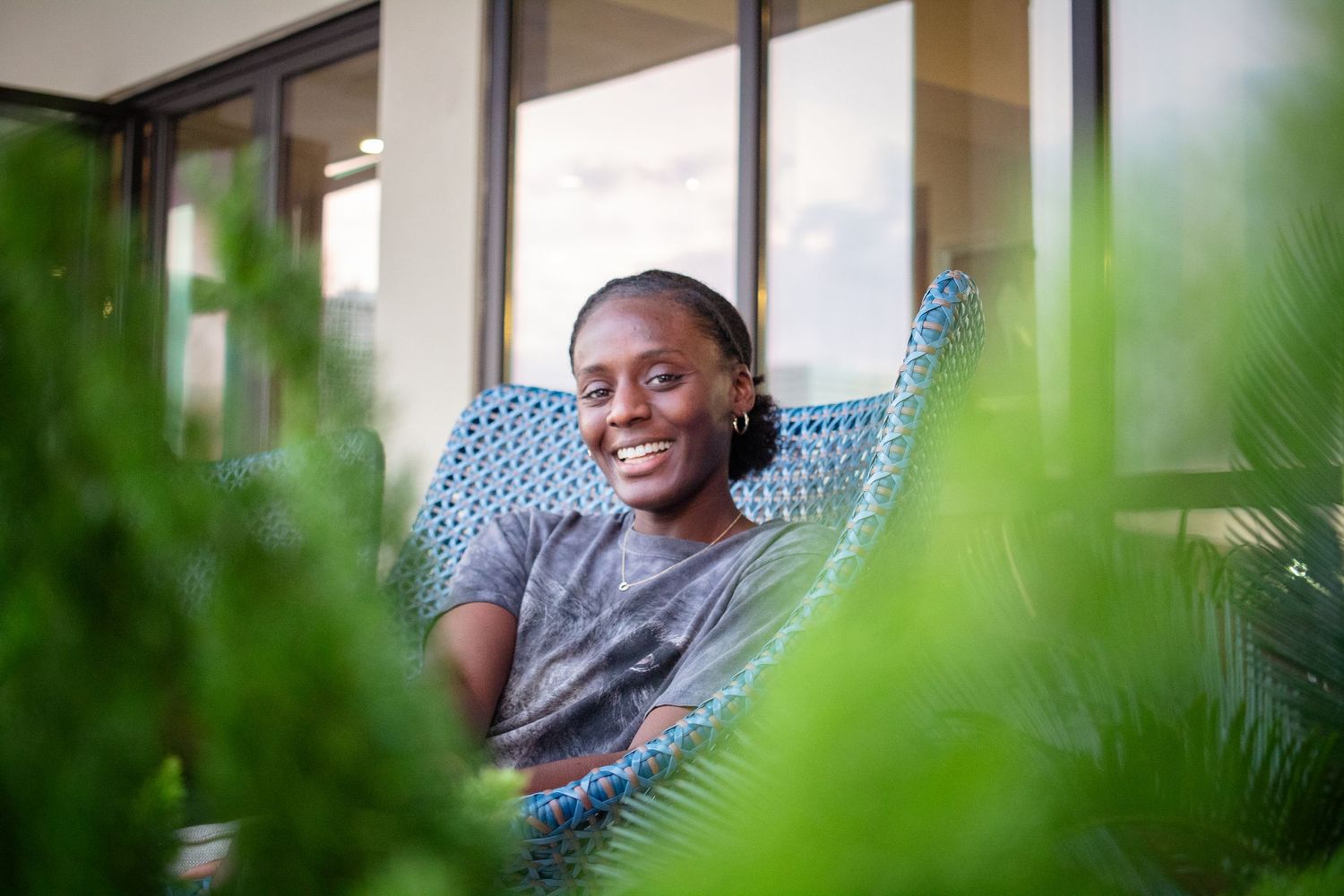 A woman laughs on a patio, surrounded by bright green shrubs.