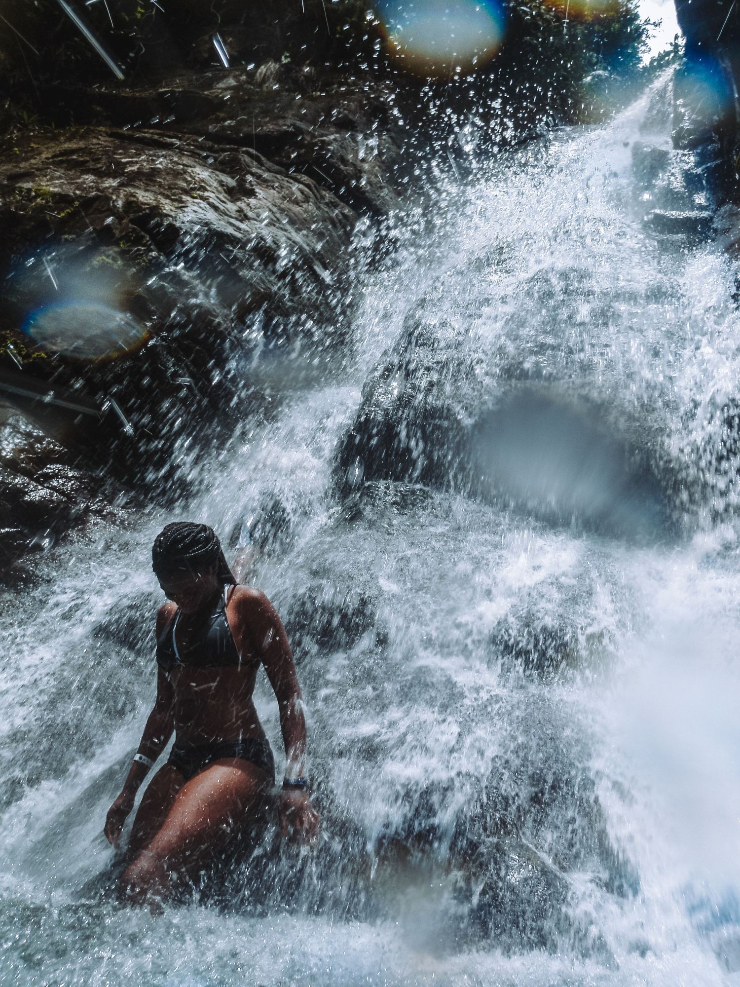 A woman sits peacefully at the base of a roaring waterfall.
