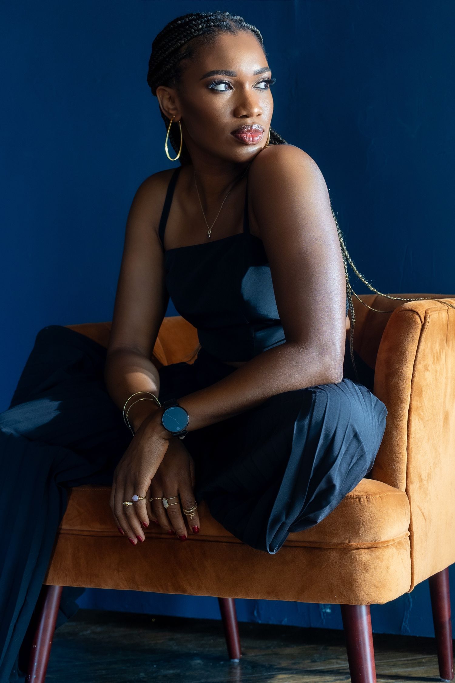 A woman in black sits on an orange chair and gazes intently away from the camera.