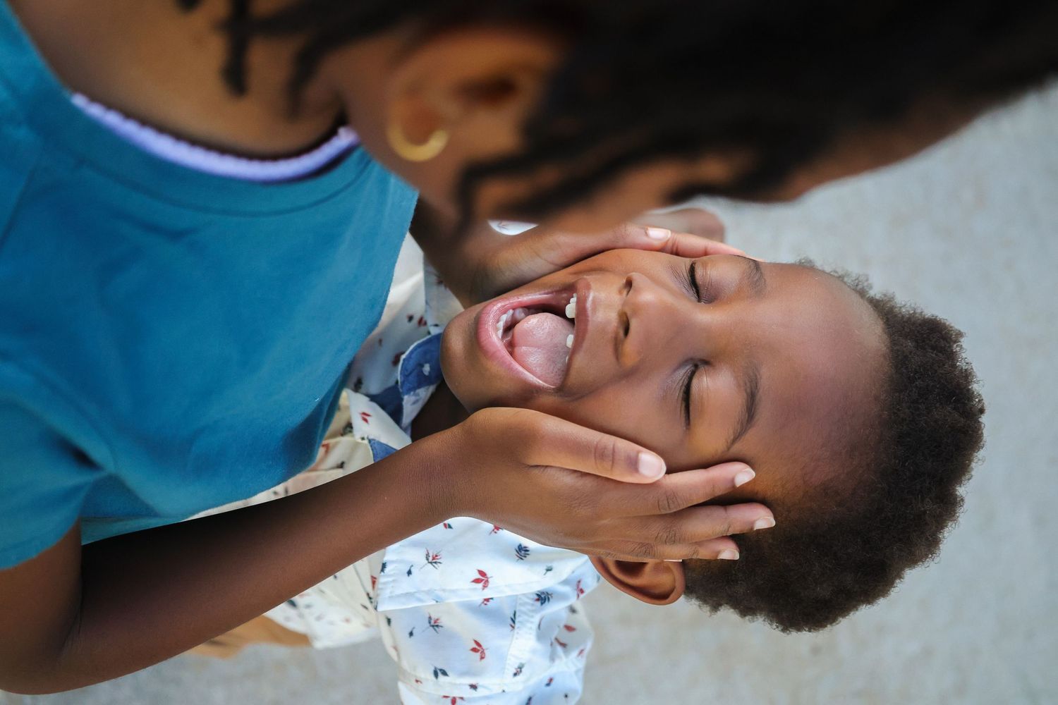 A young girl holds her younger brother's face as he sings loudly to her.