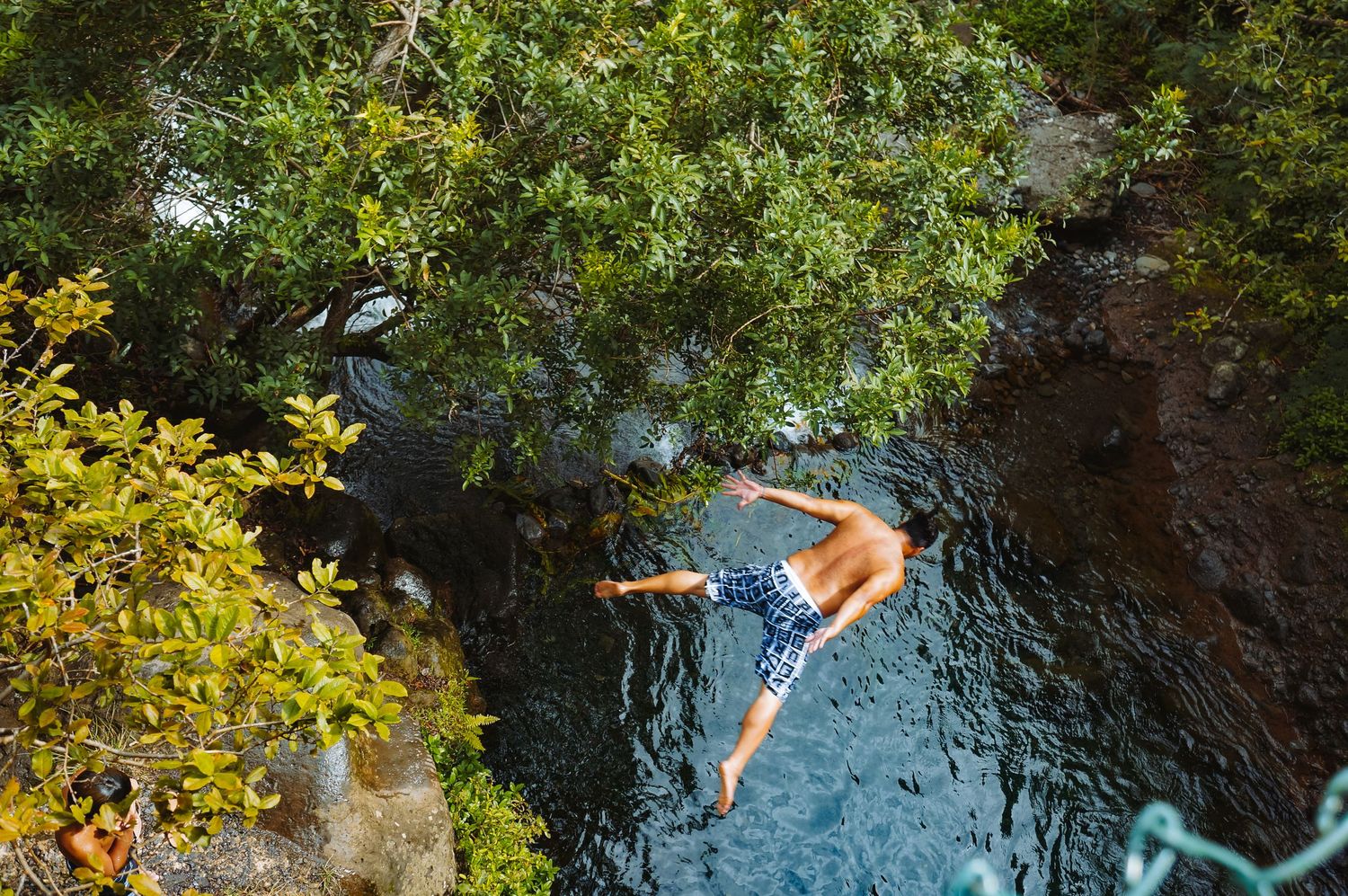A young man jumps into a rive, with eyes and legs spread wide.