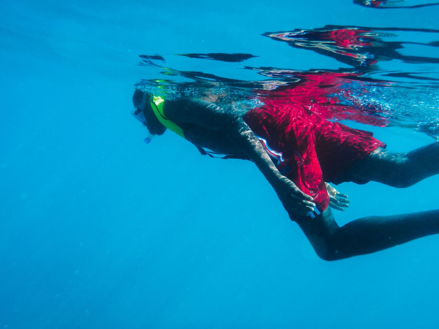 A man in bright red shorts snorkels through an endless blue expanse.