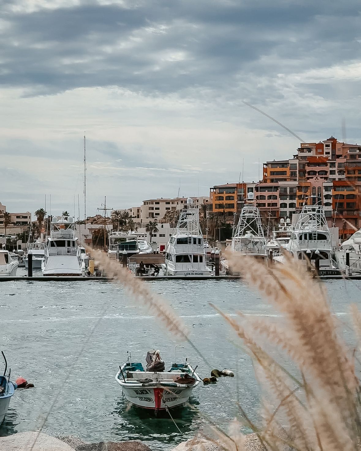 A small fishing boat rests at shore, just in front of luxury yachts and colorful high-rise buildings.