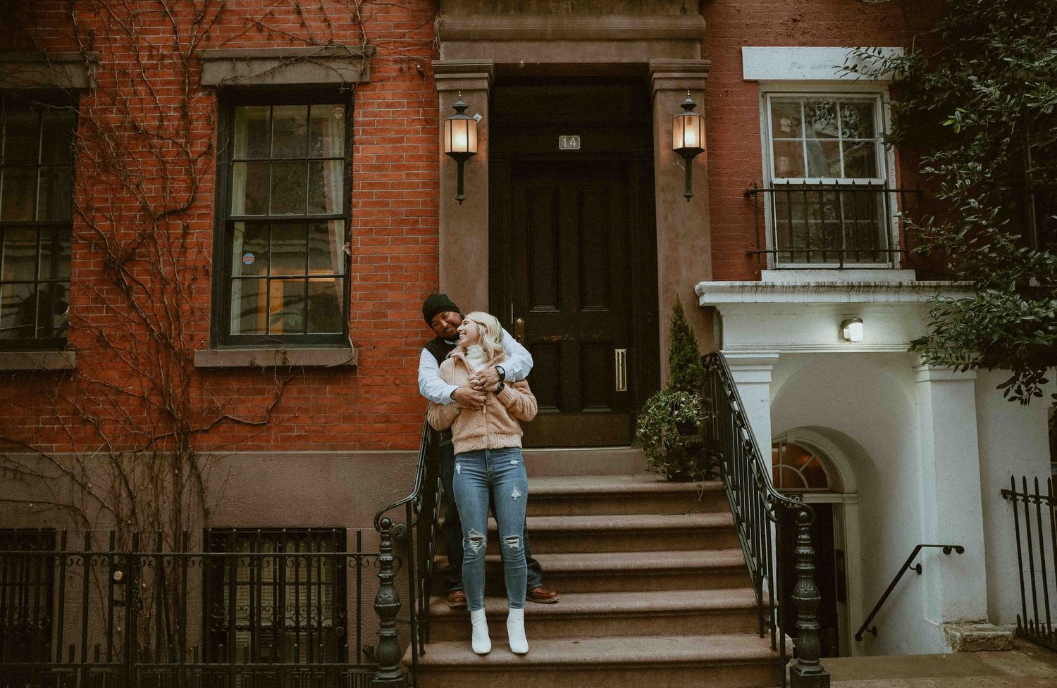 A mother holds her baby on the steps of a classic brick townhouse in an urban neighborhood, photographed by bucks county photographer
