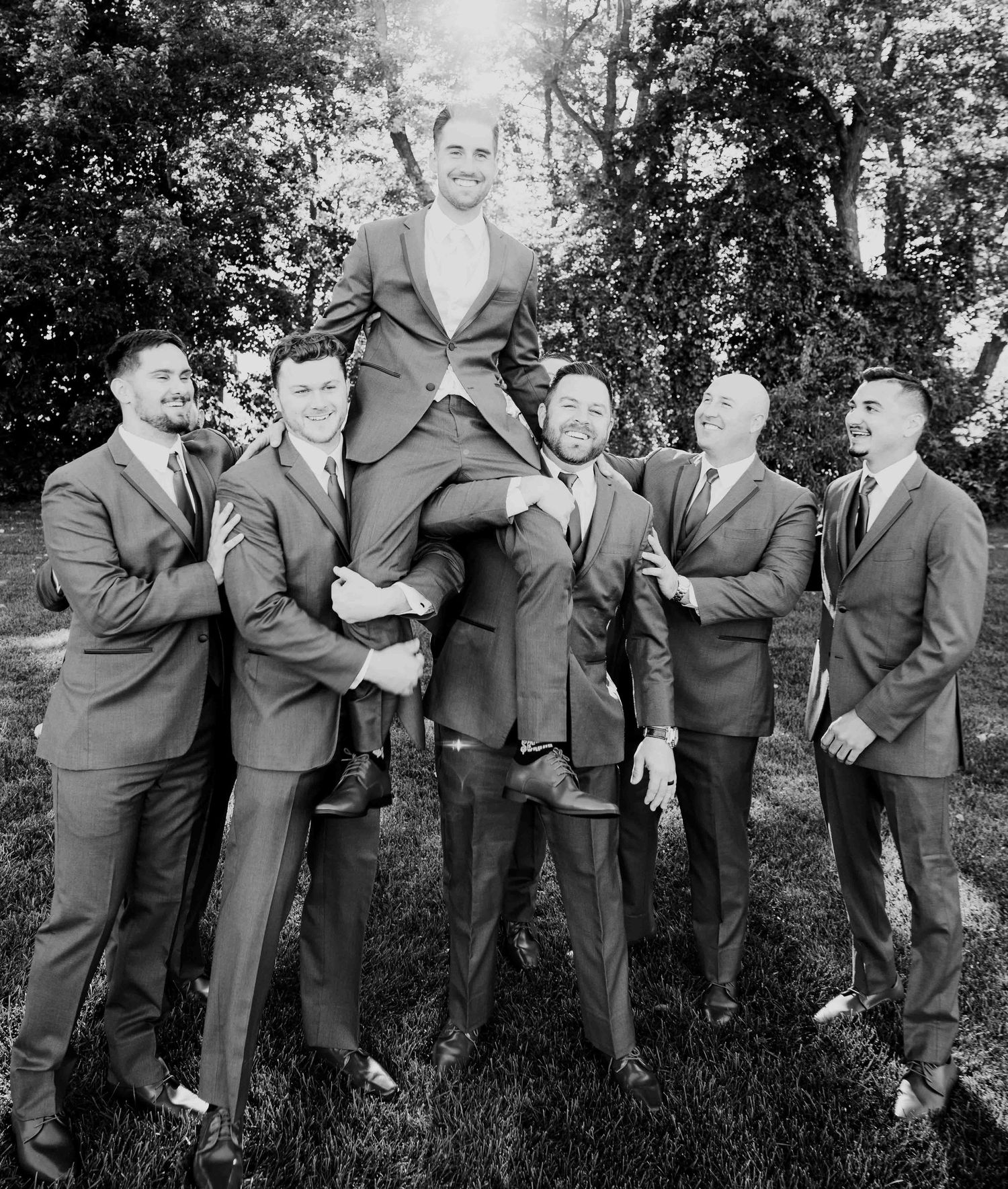 Groomsmen in matching suits lifting the groom outdoors in a black and white wedding photo. Bucks county