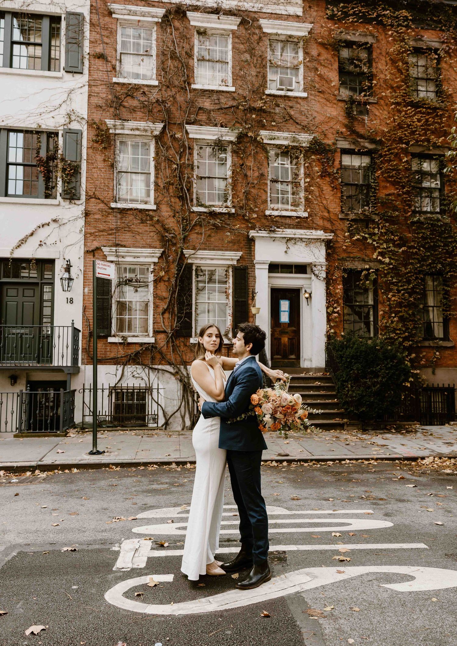 Couple embraces on a crosswalk in front of an ivy-covered brick building during an autumn wedding in New York City. Couple photographer.