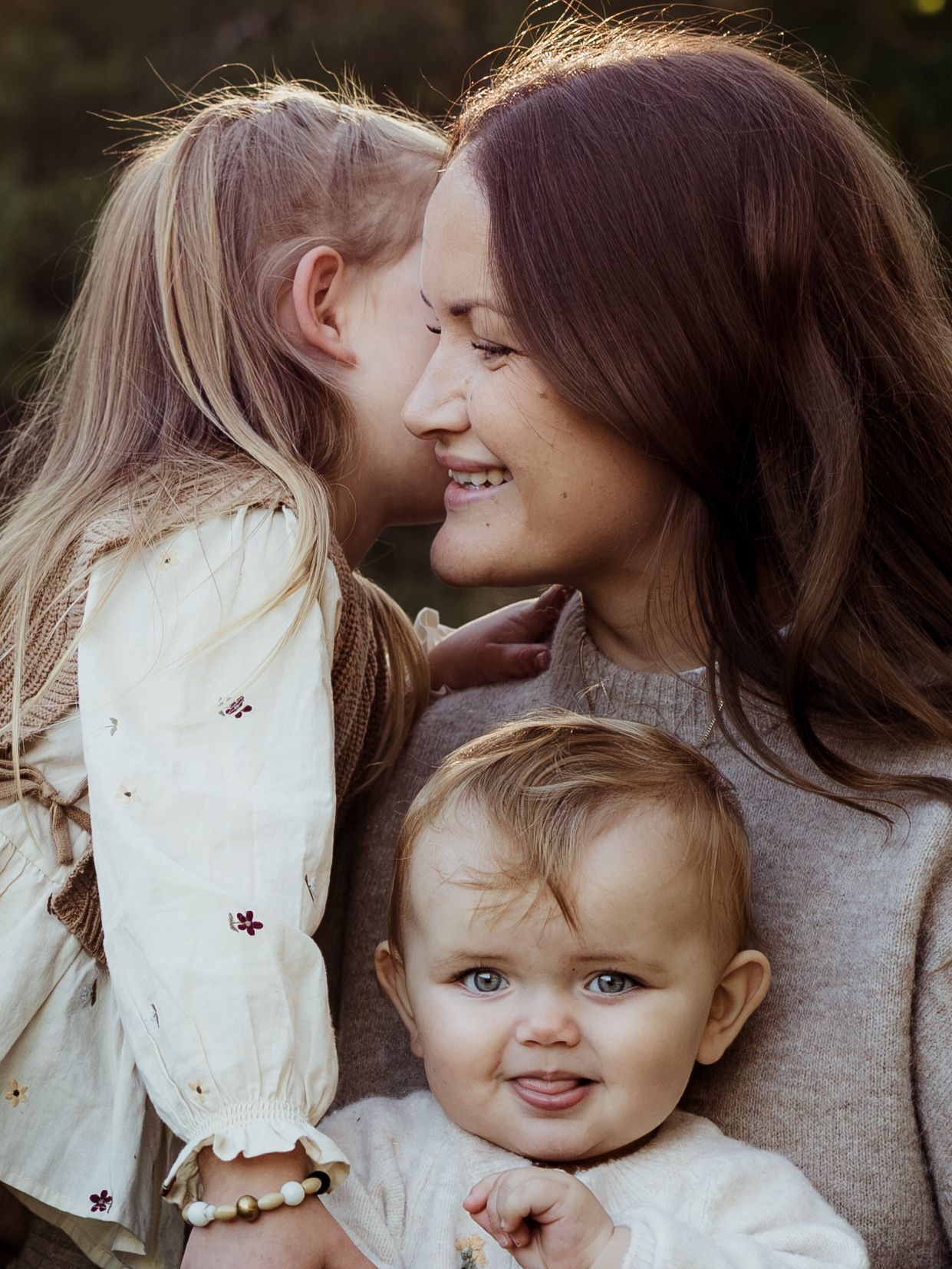 Flicka viskar i mammas öra tillsamans med lillasyster