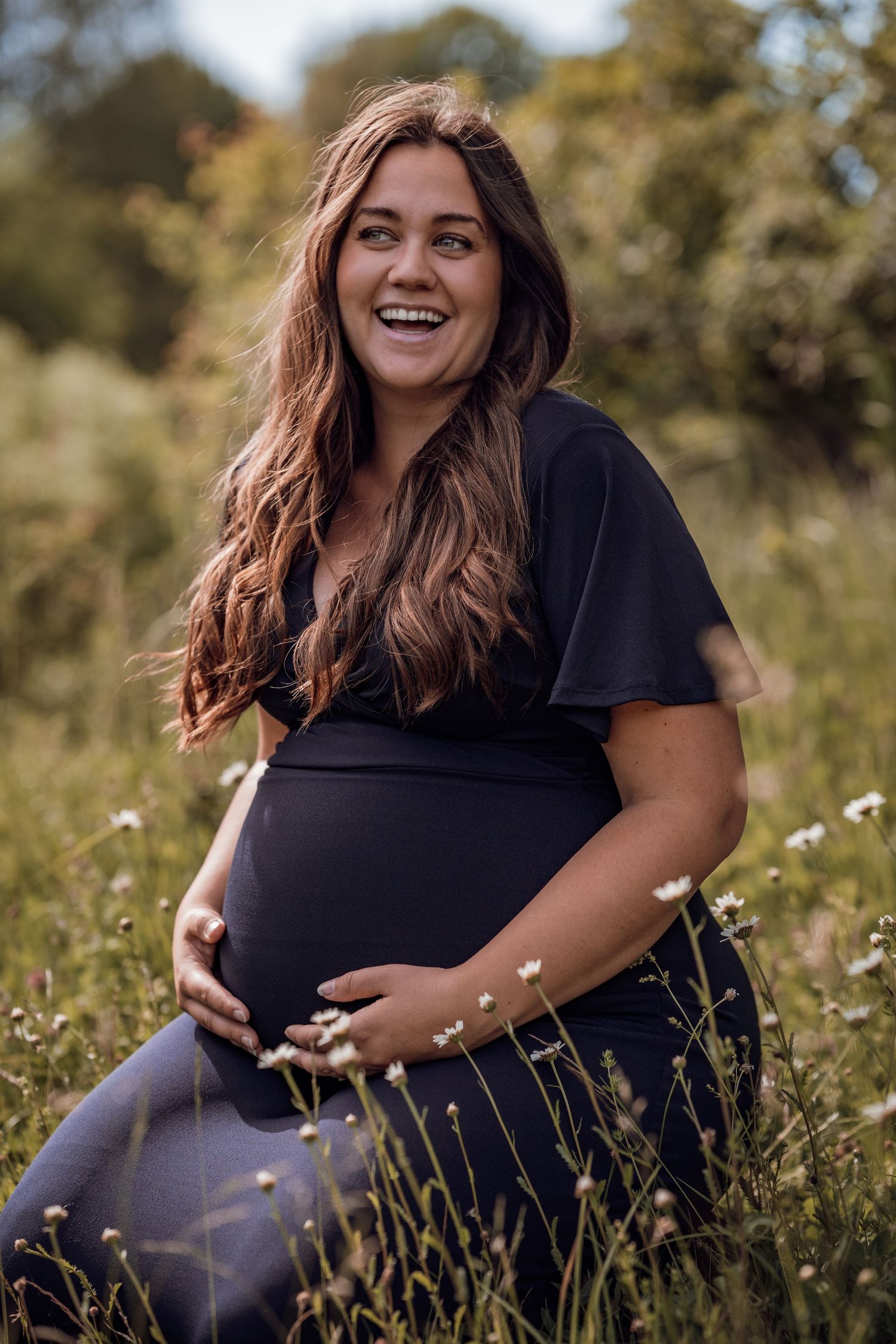 Glad gravid kvinna sittandes på en blomstrande äng