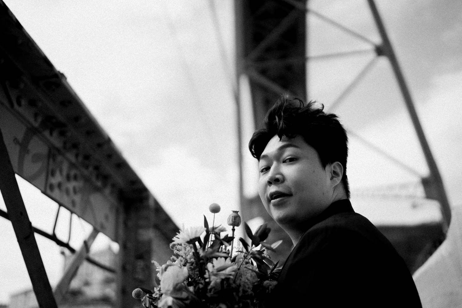 Black and white photo of a groom smiling with a bouquet under an iron bridge, during an elopement in Porto, Portugal