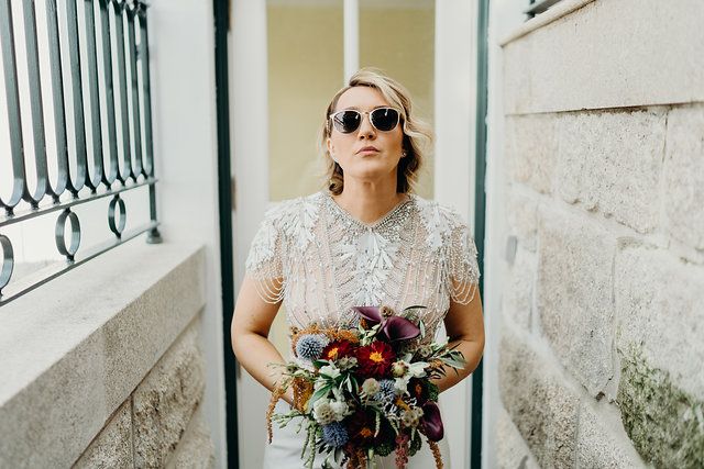 Bride in white sunglasses holding a bouquet in a narrow alley