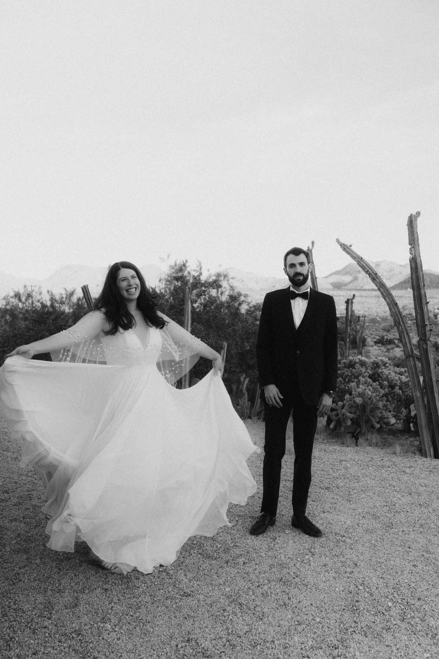 Black and white photo of a bride twirling in a full skirt beside a groom in a tuxedo