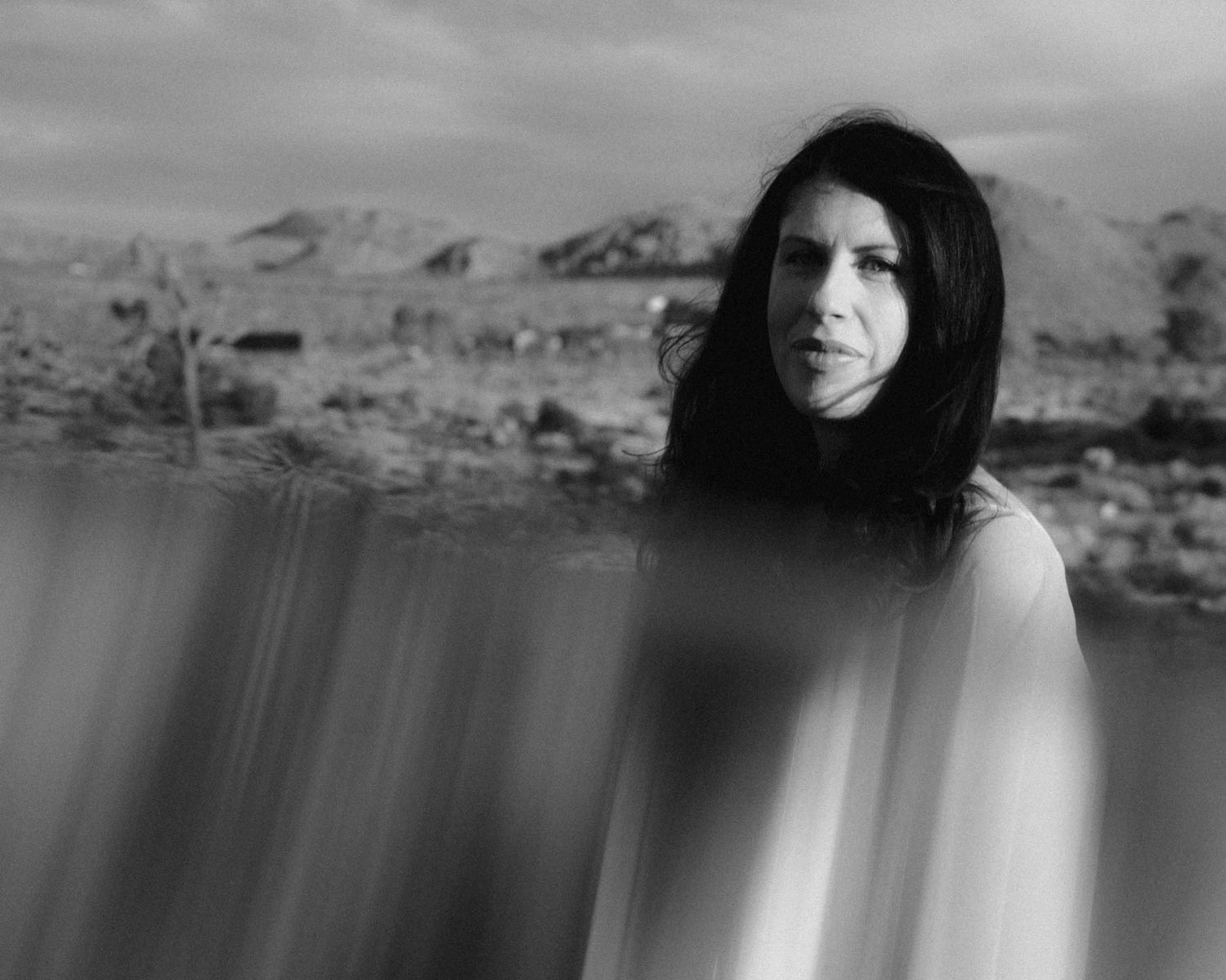 Black and white portrait of a woman with long dark hair against a desert landscape