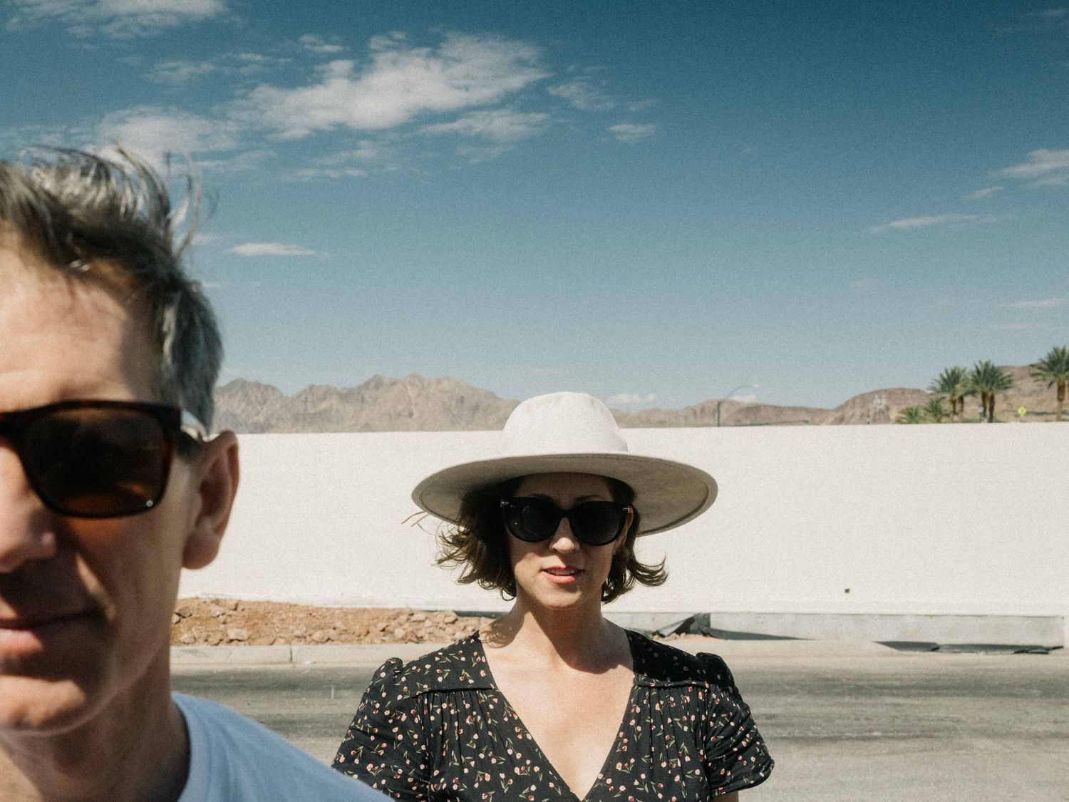 Two people in sunglasses, one in a straw hat, under a blue desert sky