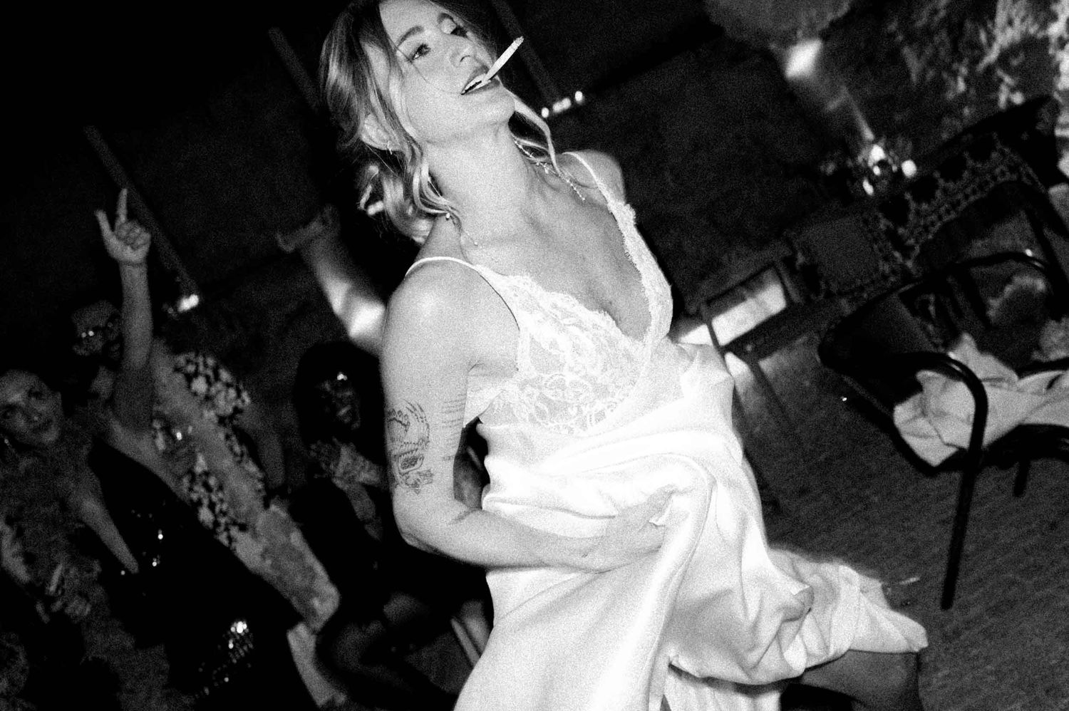 Black and white photo of a bride dancing with a cigarette in her mouth at her wedding party