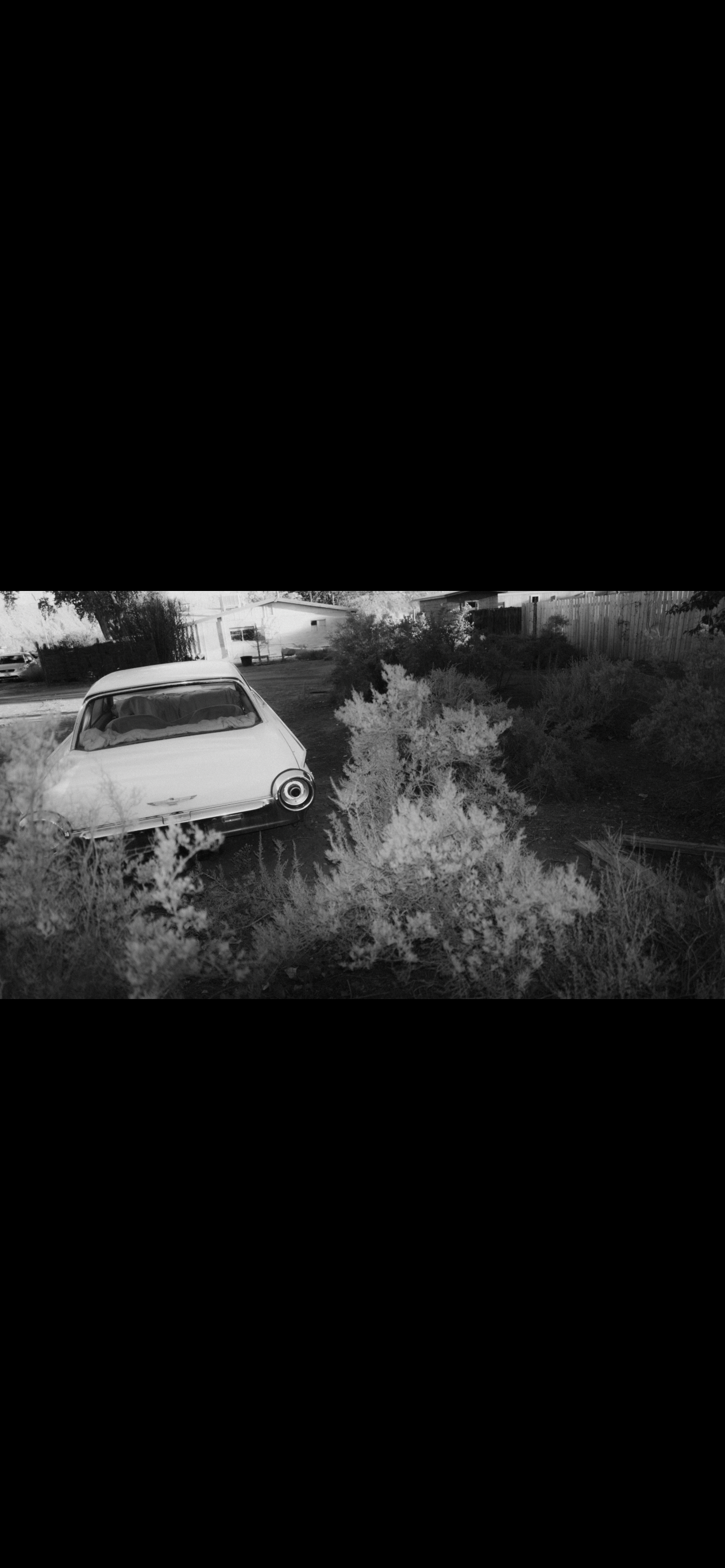 Black and white photo of a parked vintage car among desert scrub