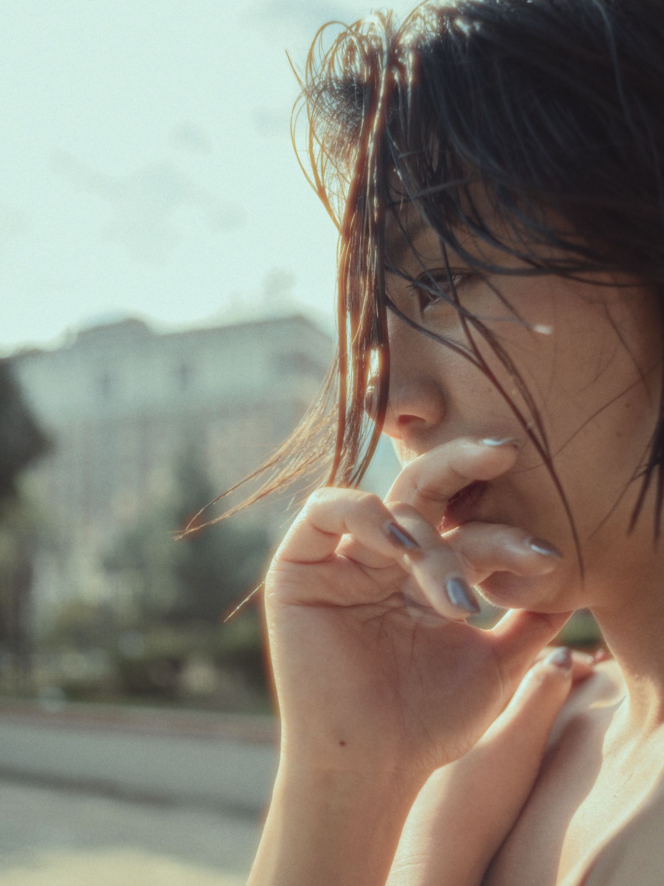 Close-up profile of a woman with windblown hair and her hand held to her mouth.