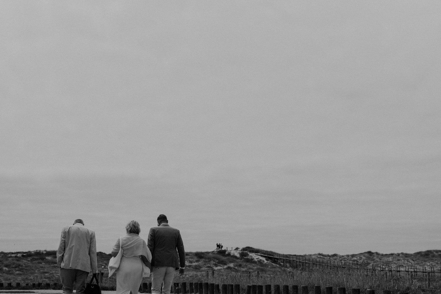 groom walks with his parents towards the beach at Set Lounge, Portugal. German-style destination wedding cinematic photography