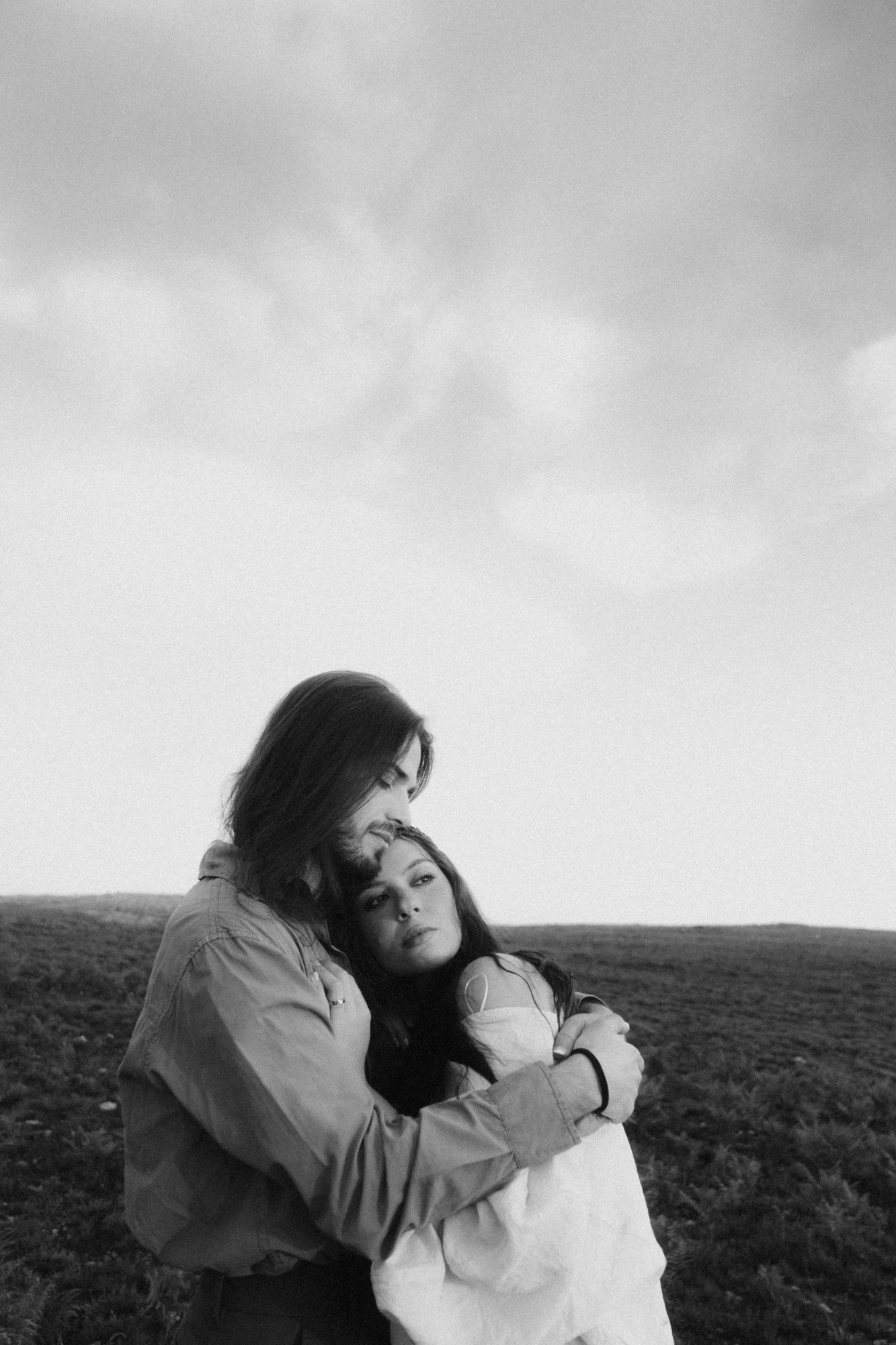 Black and white portrait of a couple embracing in an open field.
