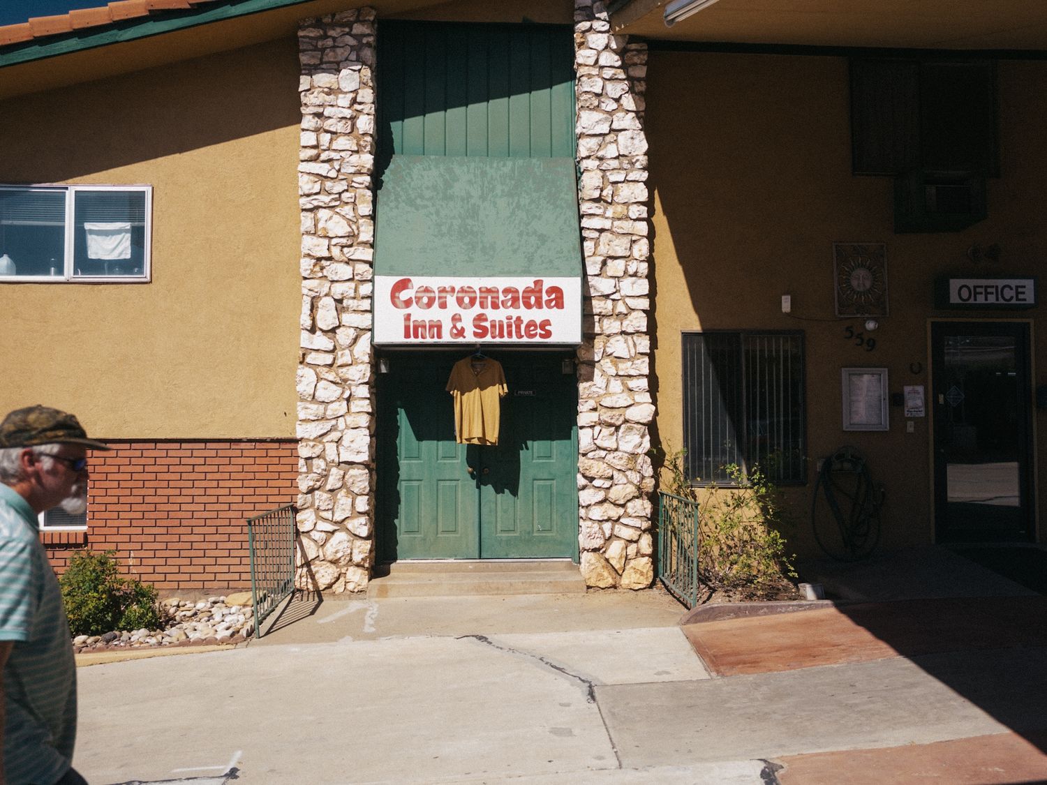 Motel entrance with stone columns and green doors under a sign.