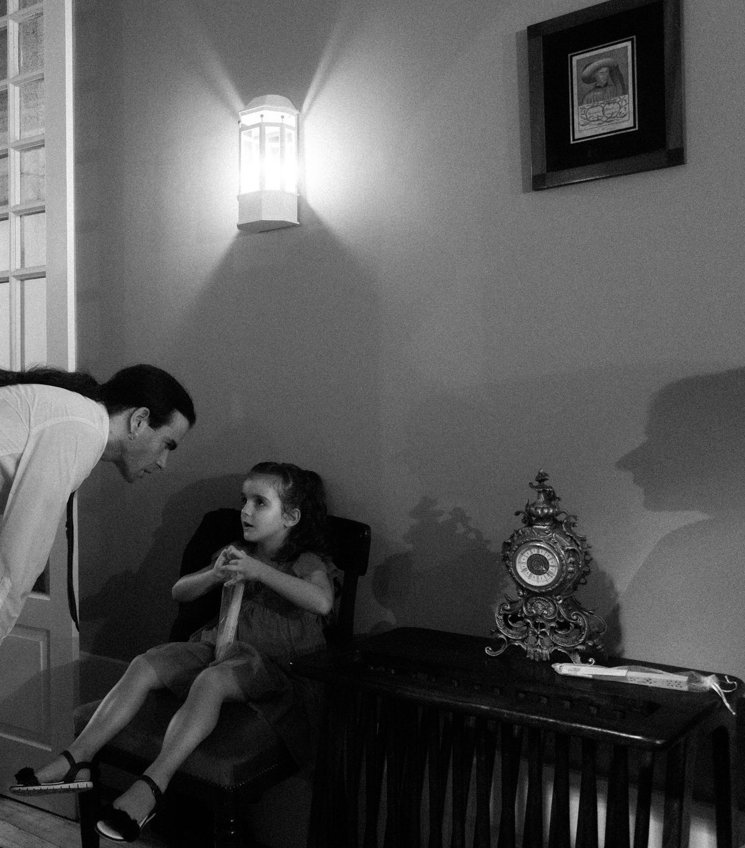Two people in a dim room lit by a wall lamp