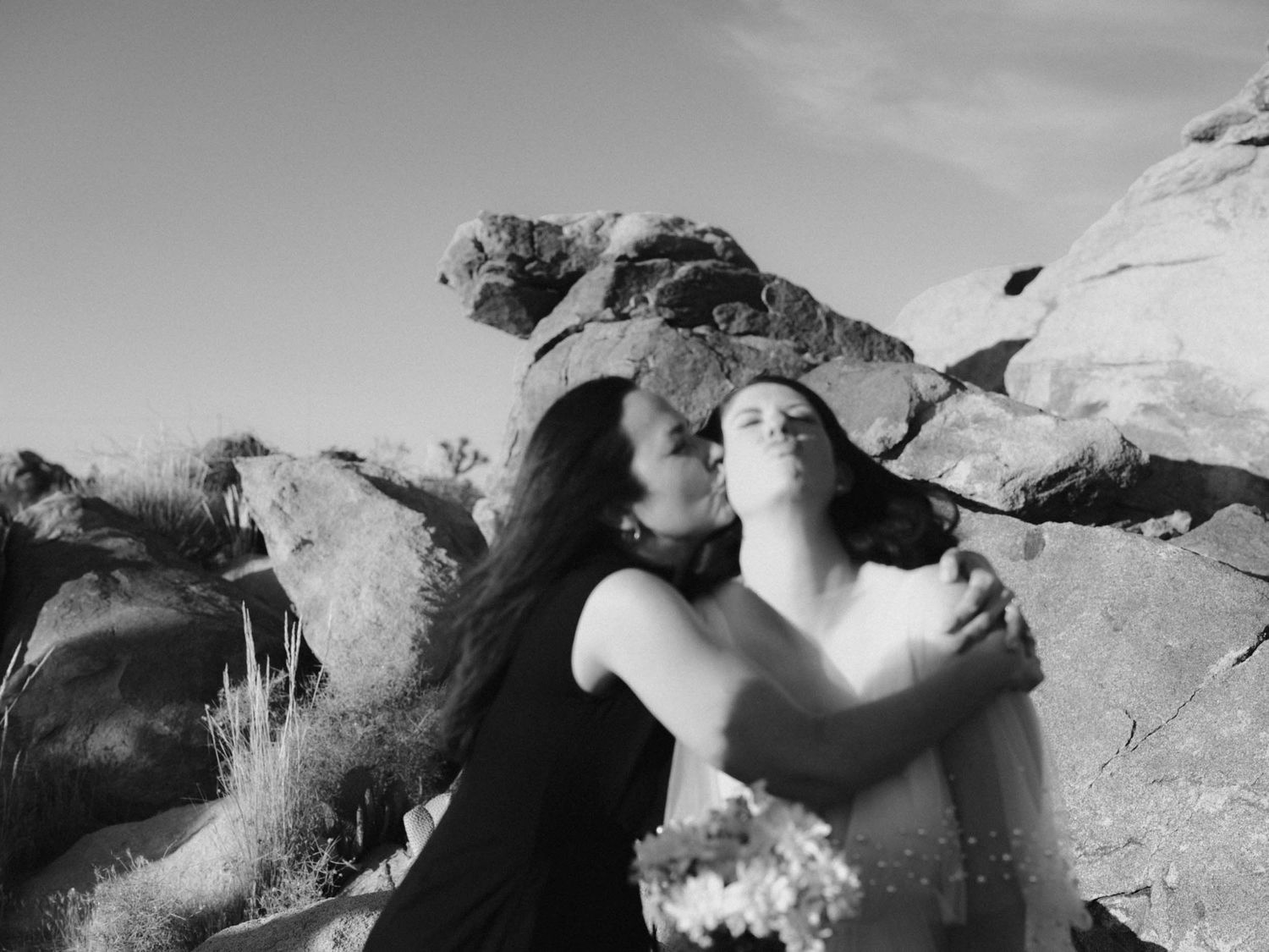 Black and white photo of two people embracing among large desert boulders