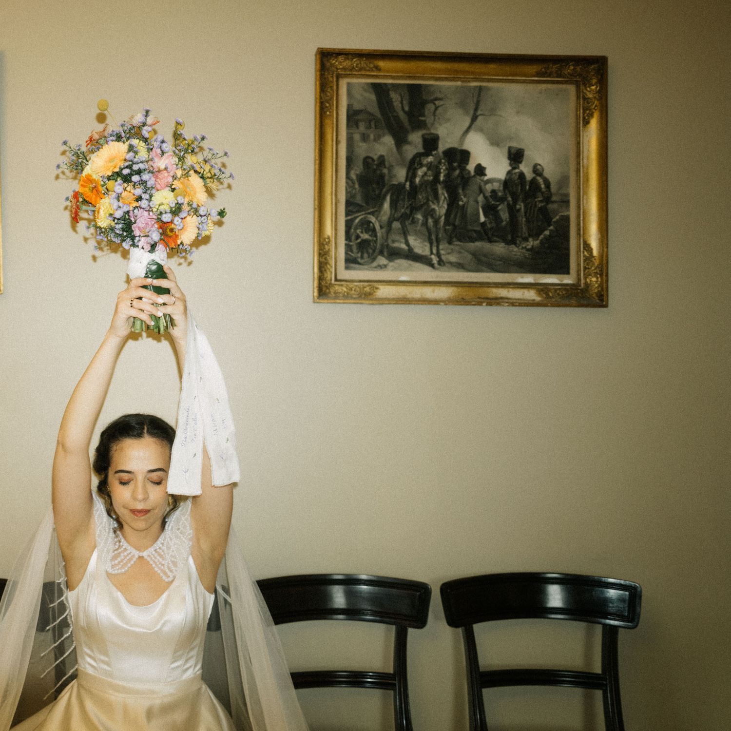 Bride throwing her bouquet in a room with a framed painting on the wall