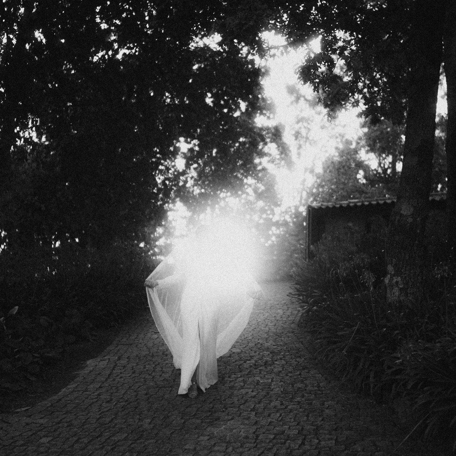 Black and white photo of a bride walking away down a dark path into a burst of light