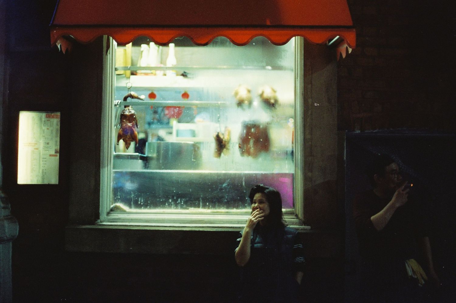 A woman in front of a lit shop window at night