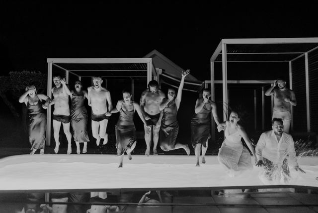 Black and white photo of wedding guests jumping into a pool at night