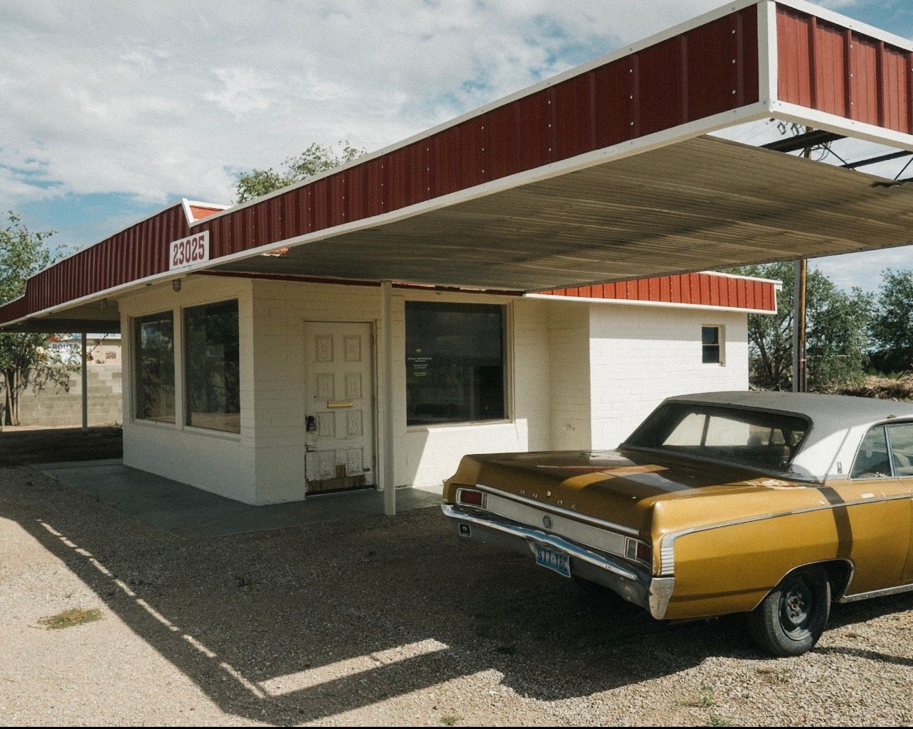 Red-roofed roadside gas station with a gold vintage car parked in front under blue sky