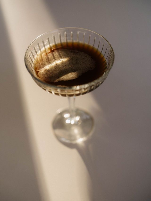 Coupe glass with a dark drink in a beam of light.