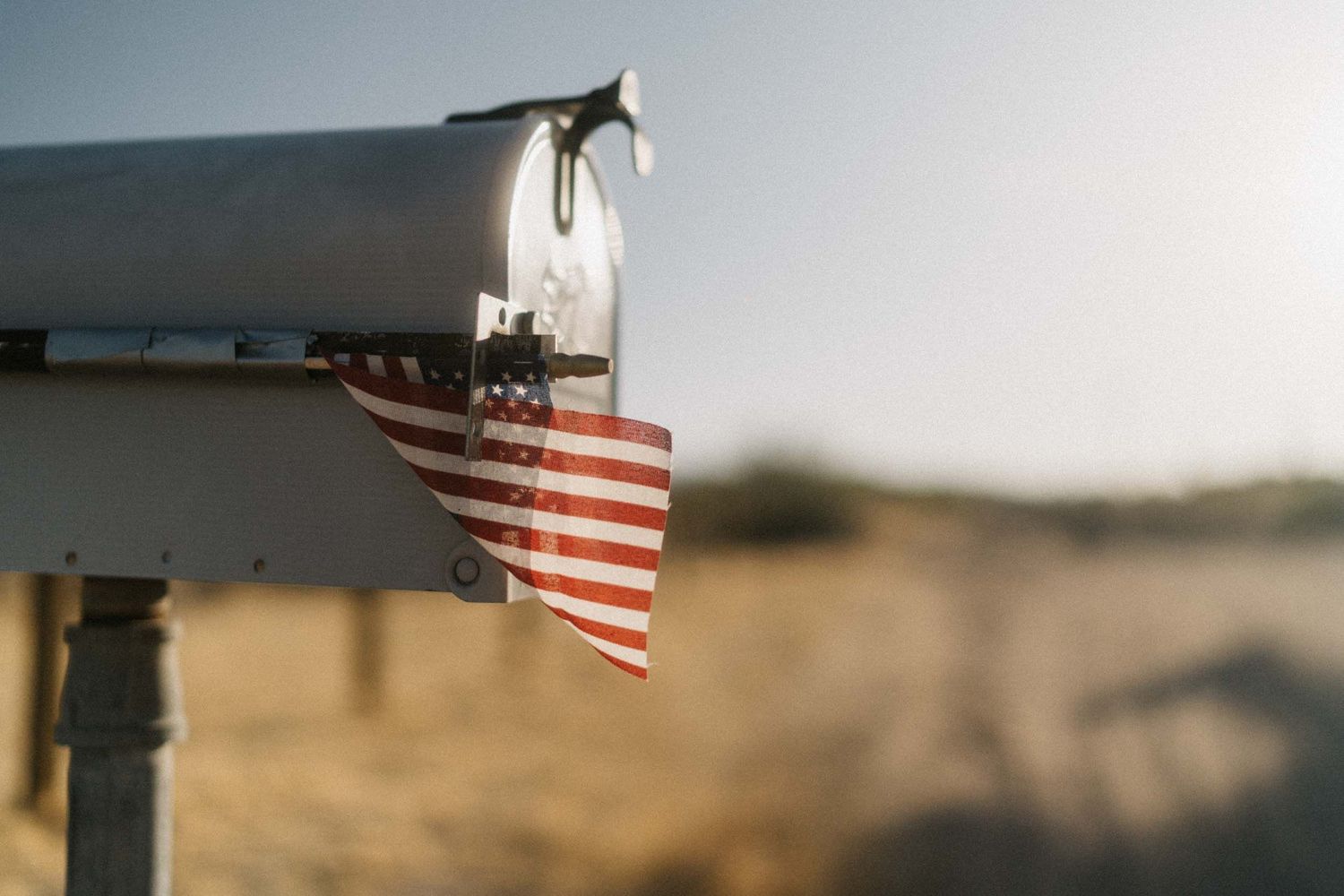 Mailbox with an American flag in a dry desert field, soft-focus background