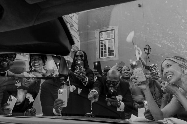 Black and white photo of wedding guests laughing behind a car window