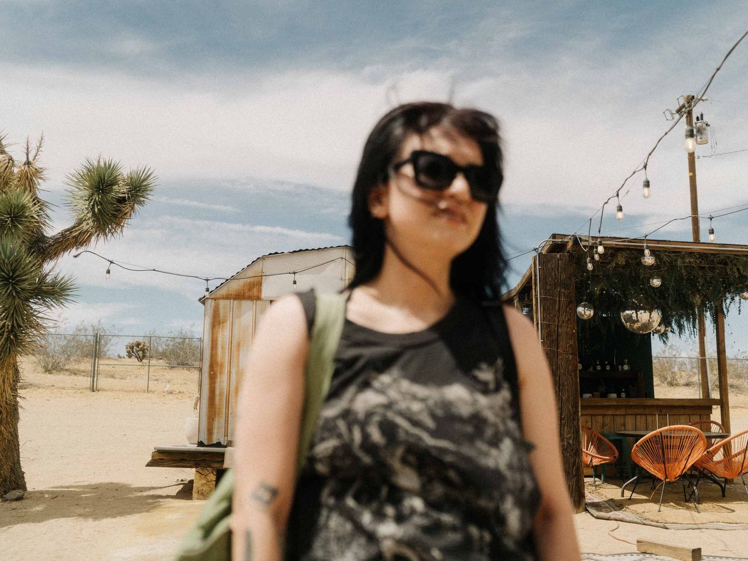 Woman in sunglasses and a camouflage top in front of a desert trailer with Joshua trees