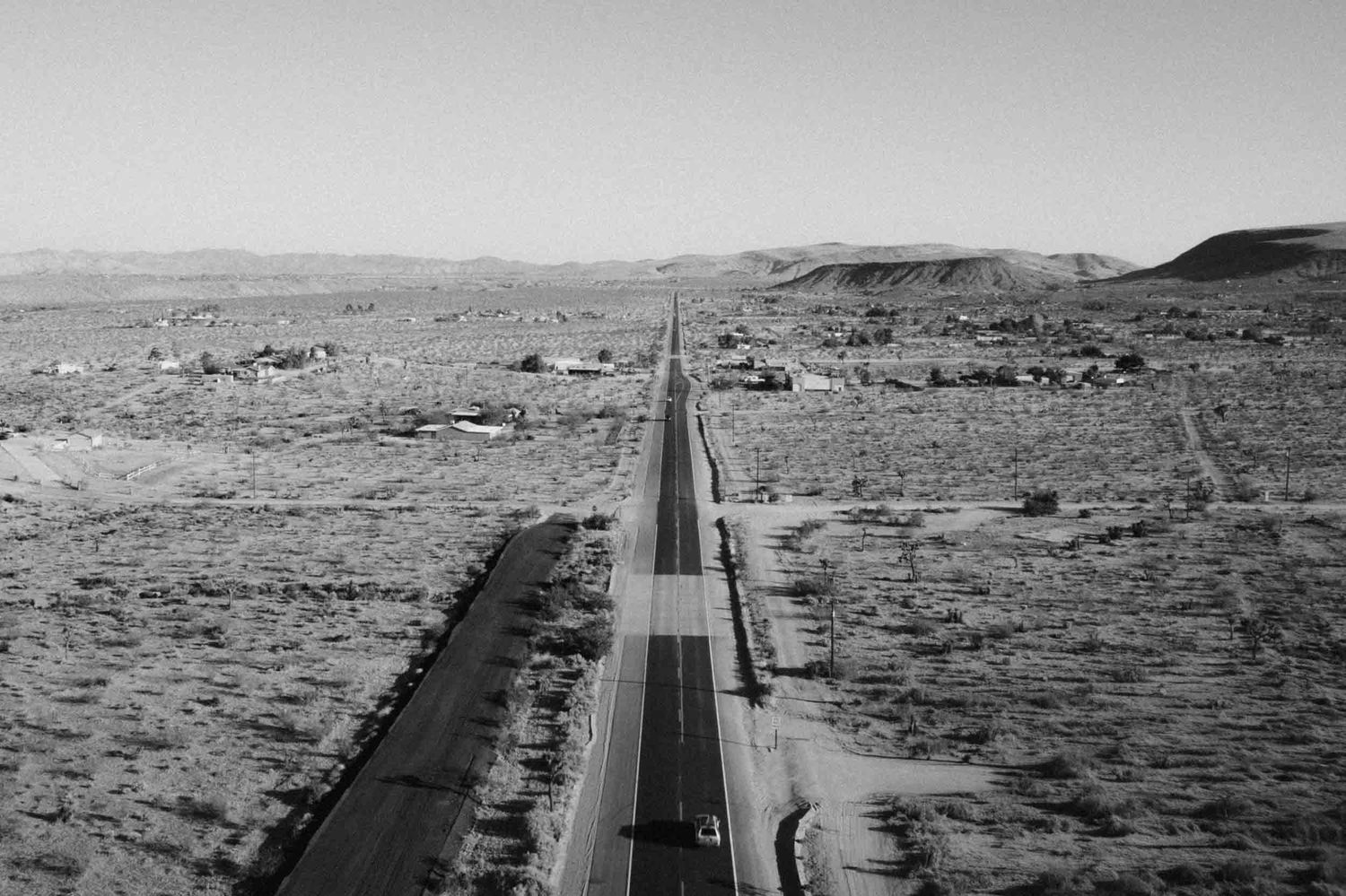 Black and white aerial view of a straight desert road running toward distant hills