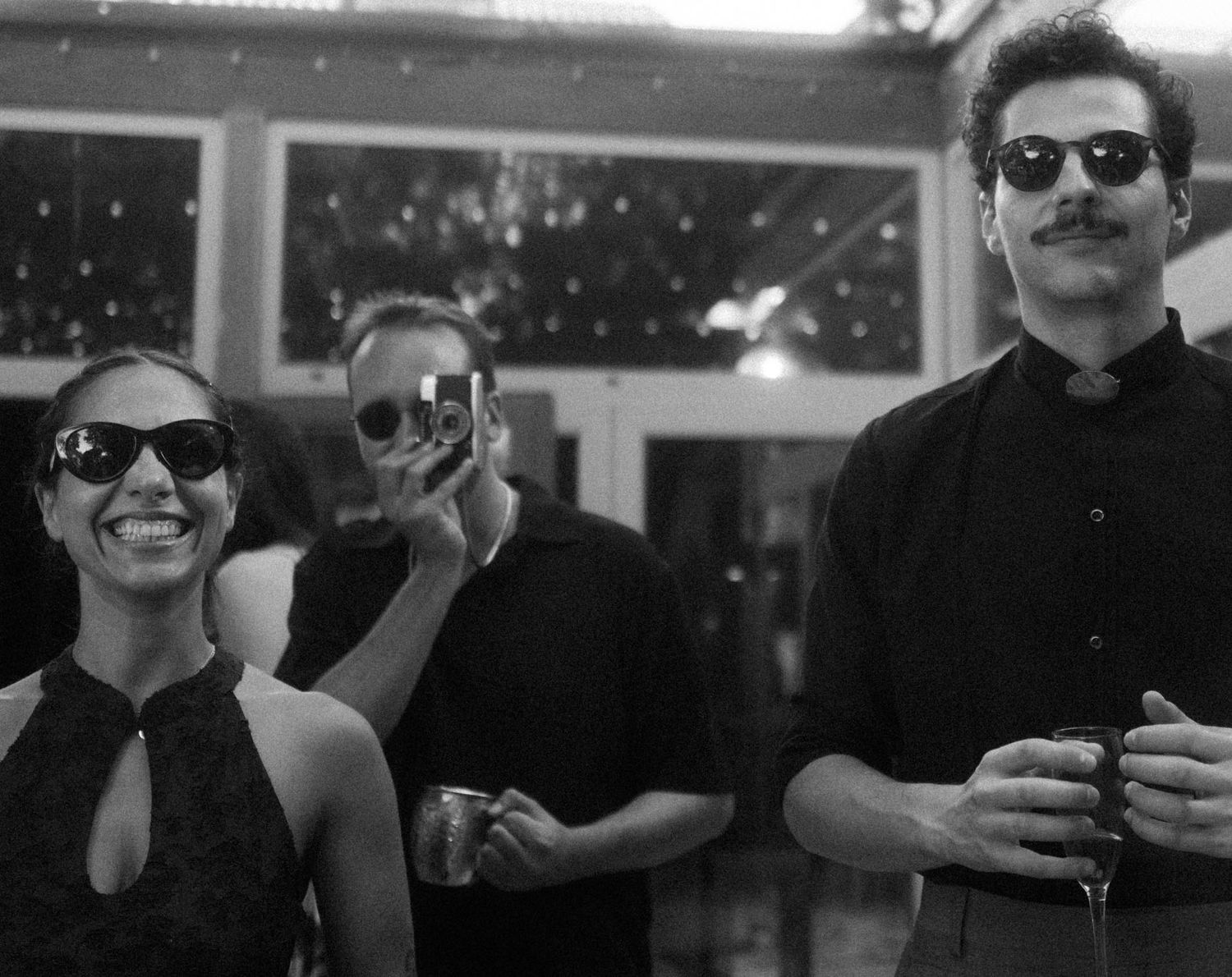 Black and white photo of wedding guests in sunglasses laughing together