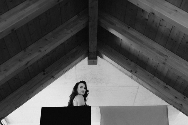 Black and white photo of a woman speaking at a lectern under a pitched wooden roof