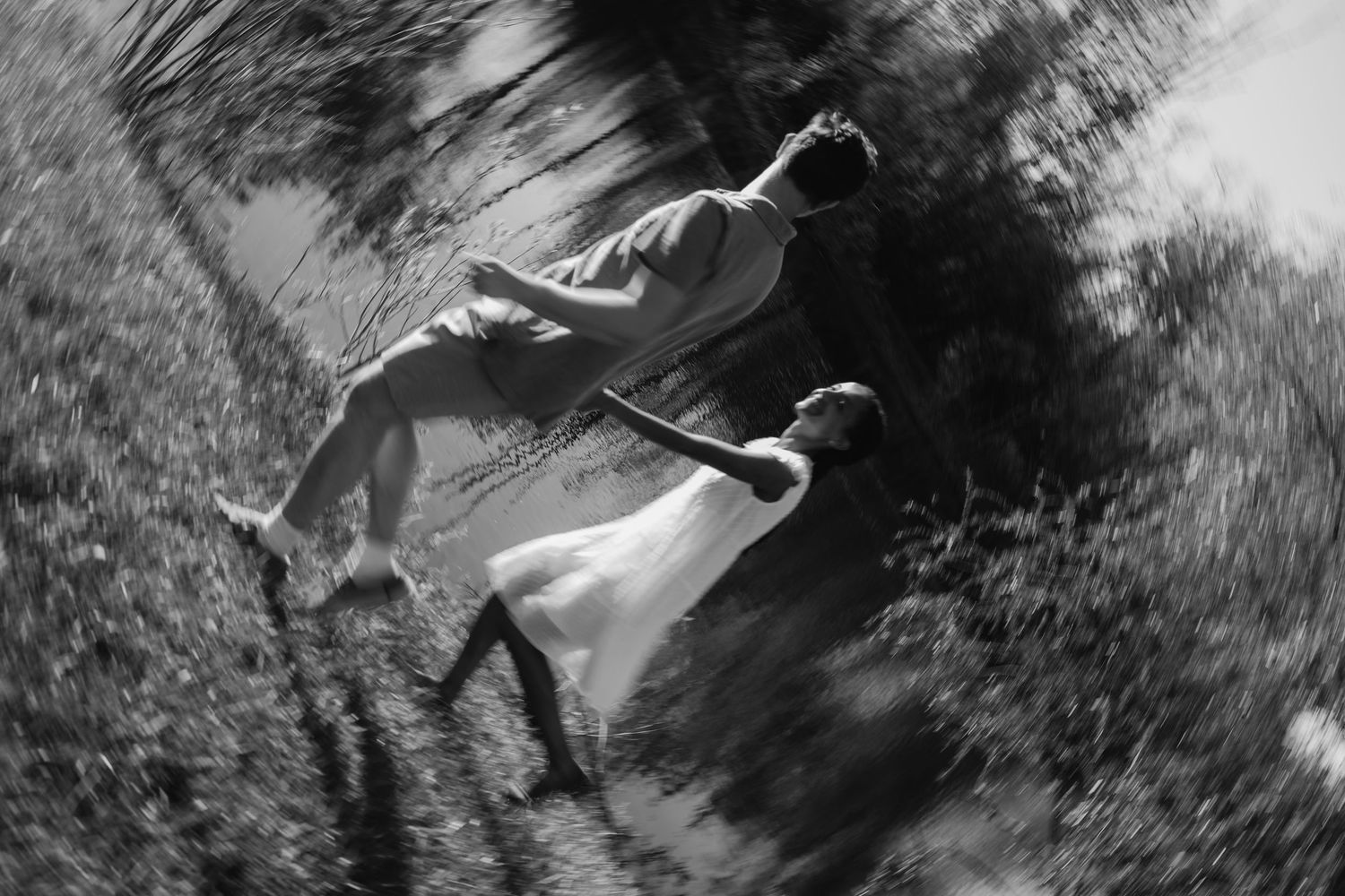 Black and white artistic blurred photo of a couple holding hands running through a lush green forest path.