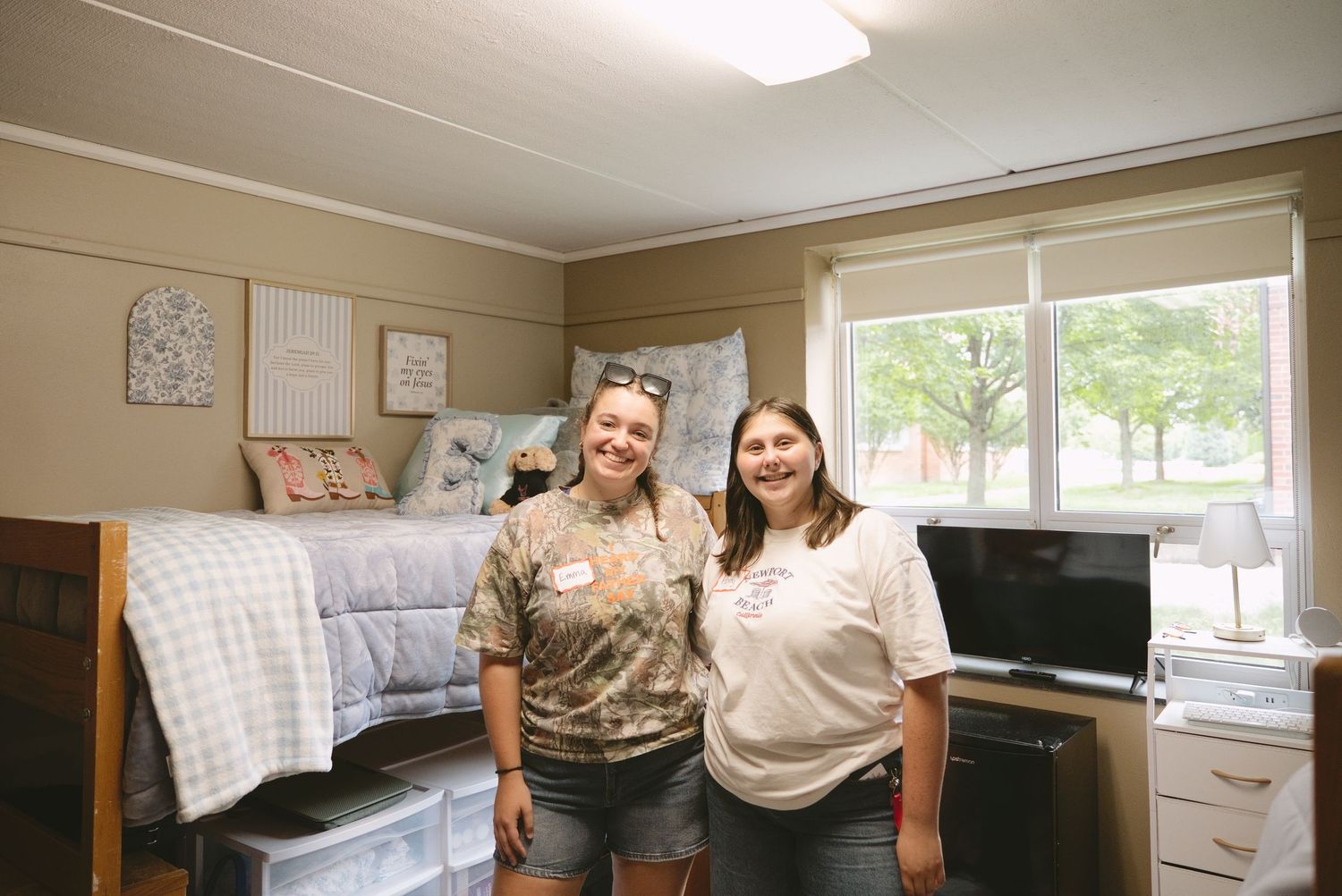 Two smiling college students pose together in a decorated dorm room during move-in day.