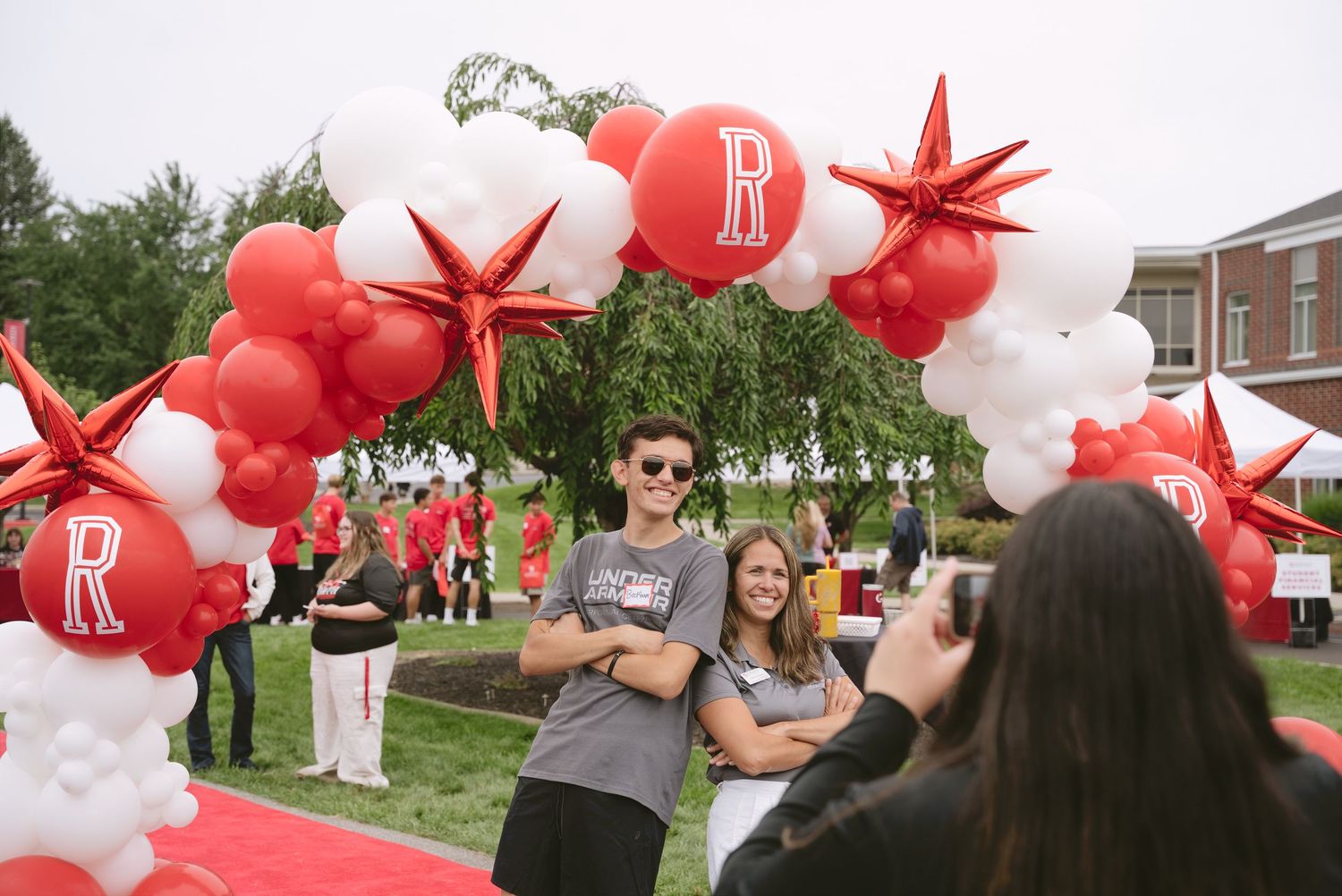 Two students pose under a red and white balloon arch at a Roberts Wesleyan University campus event.