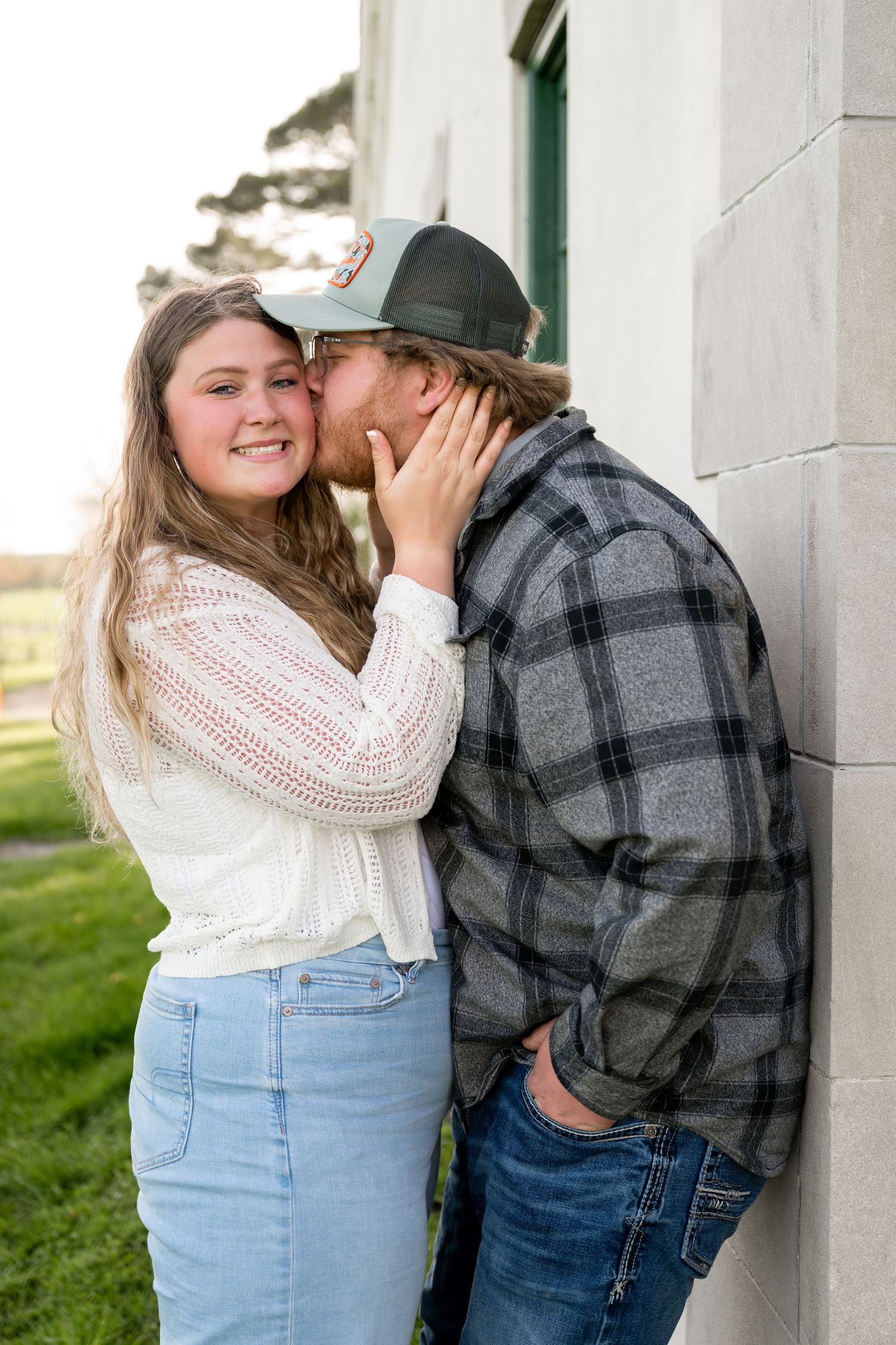 Couple sharing a kiss against a stone wall during outdoor engagement photo session.