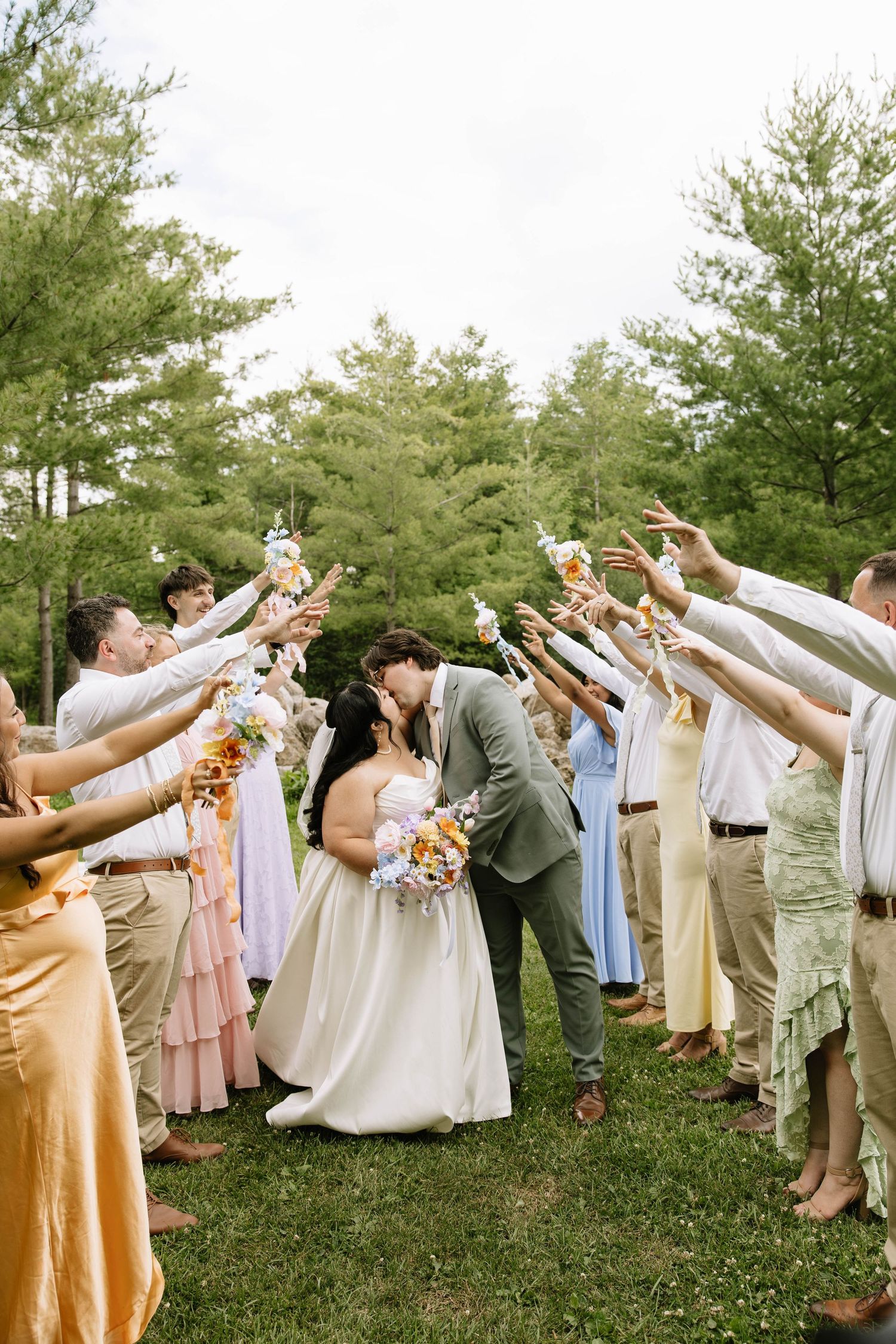 Bride and groom kissing under an arch of raised glasses during outdoor wedding send-off.