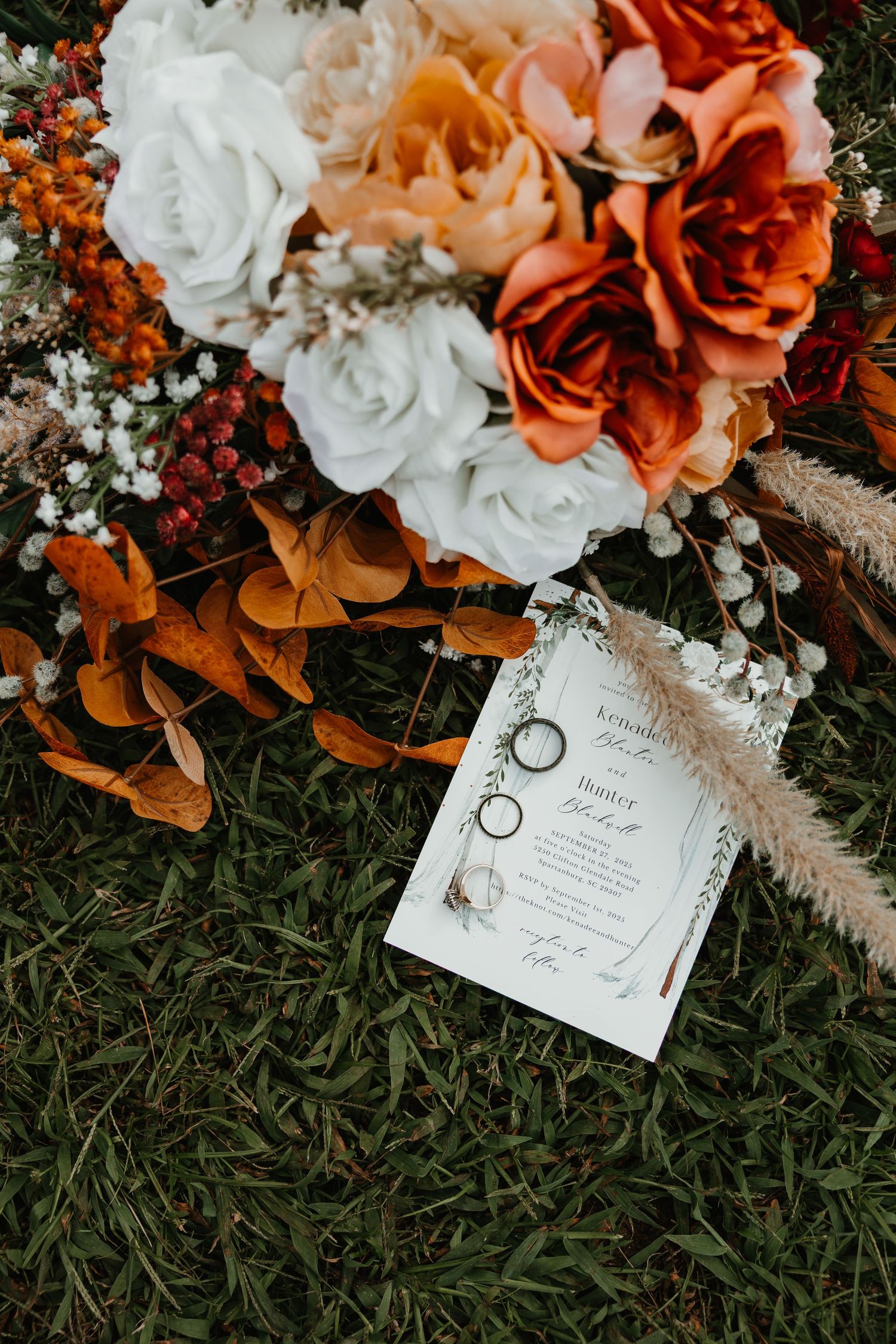 Wedding invitation cards nestled among peach and white roses with delicate baby's breath flowers on grass.